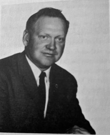 Black and white portrait of a man in a suit and tie, posing with his hands folded.