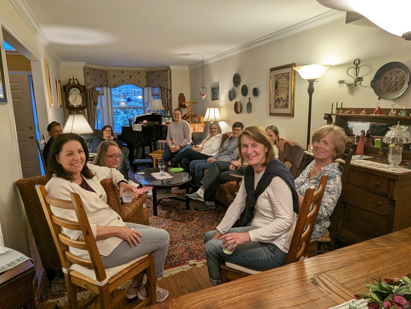 A group of ten women gathered in a cozy living room, sitting around a coffee table and smiling at the camera.
