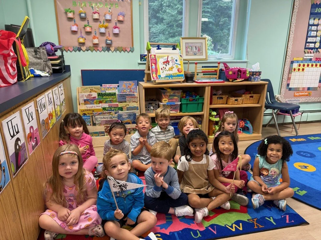 A group of young children and an adult playing in a sand table indoors.