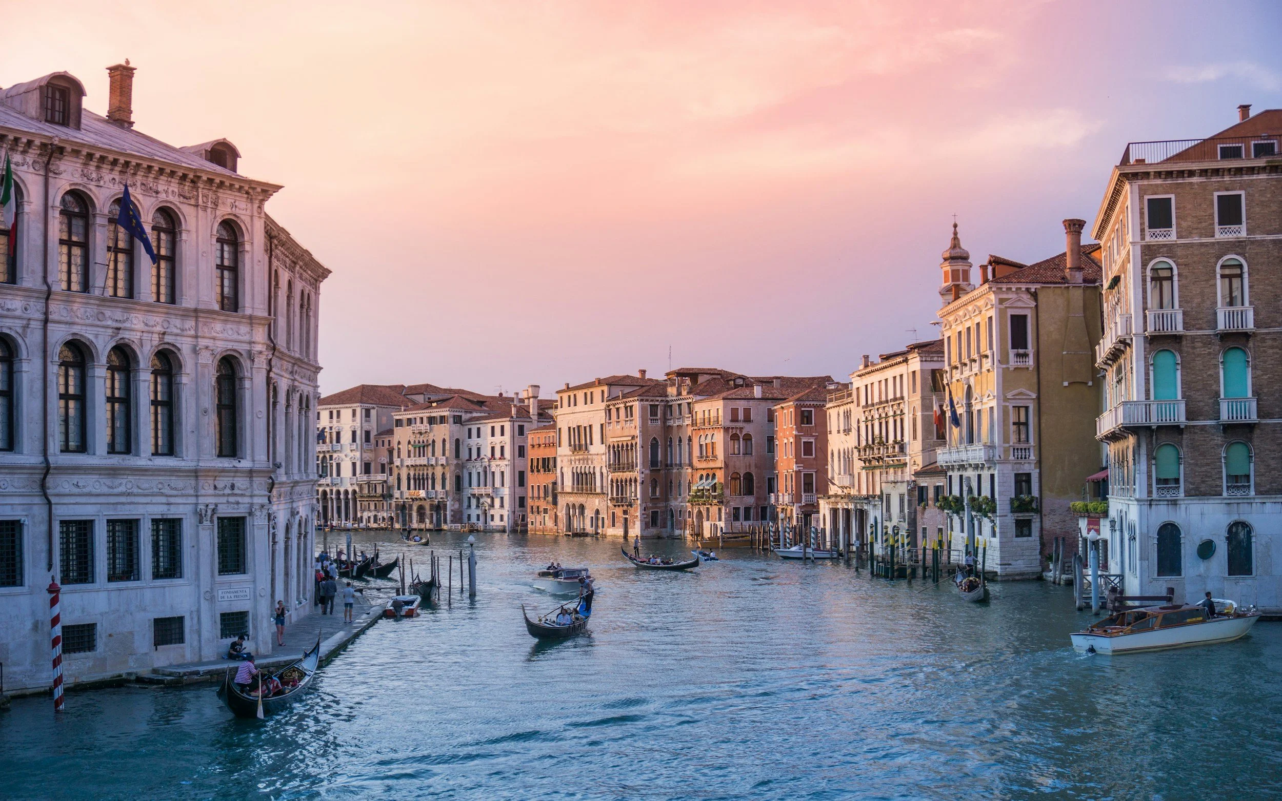 Venetian canal with gondolas and colorful historic buildings at sunset.
