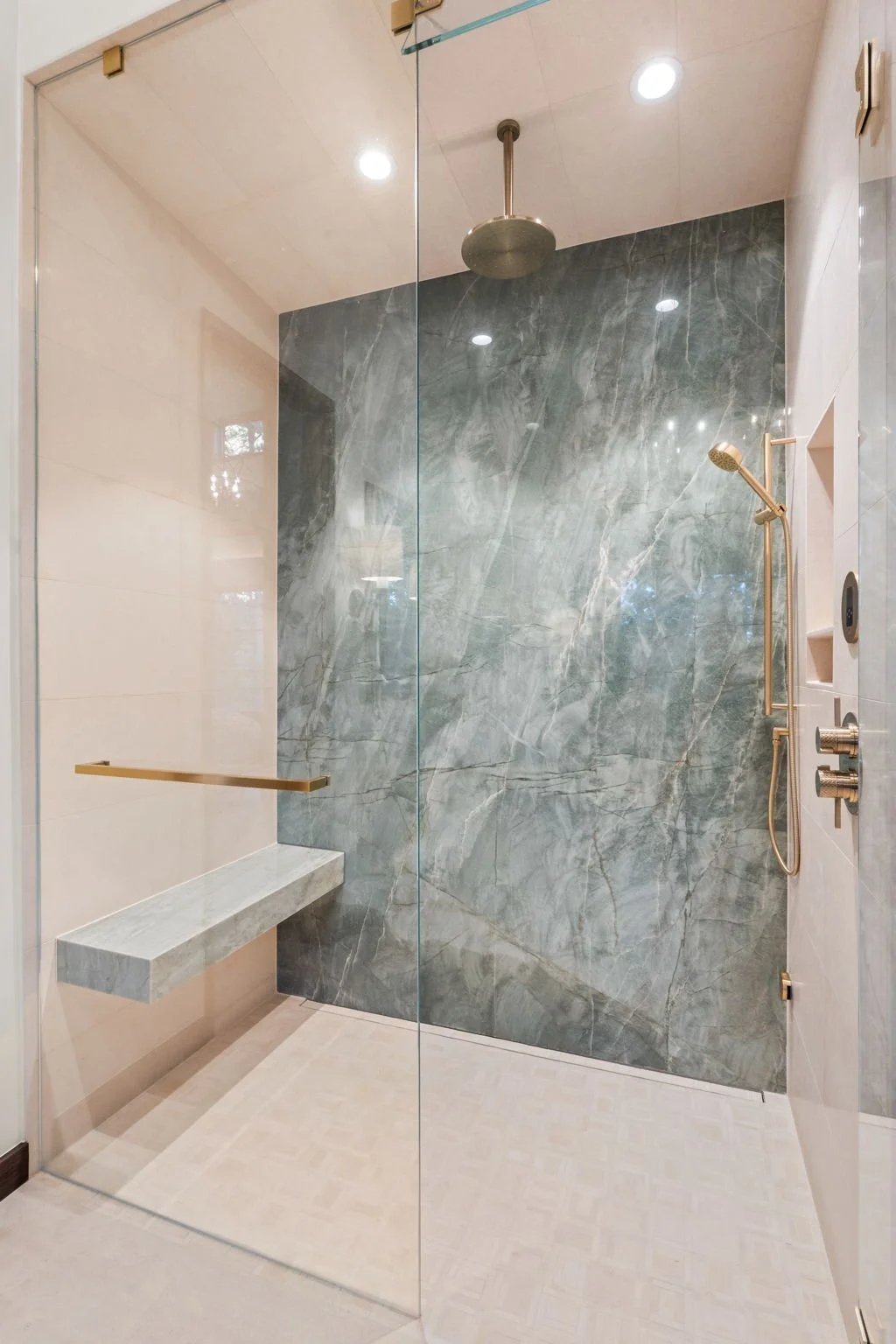 Walk-in shower at the Cedar & Stone residence in Jefferson County, Colorado, with green marble wall, brass fixtures, and glass enclosure.