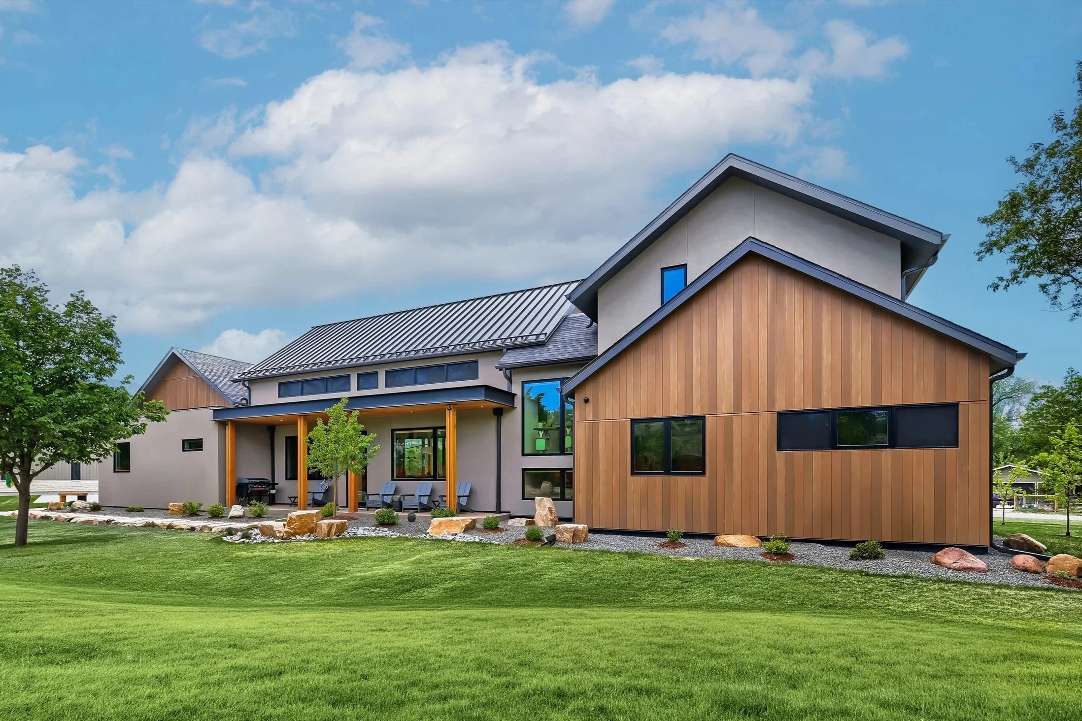 Modern farmhouse-inspired residence with wood and stone exterior, metal roof accents, and landscaped yard.