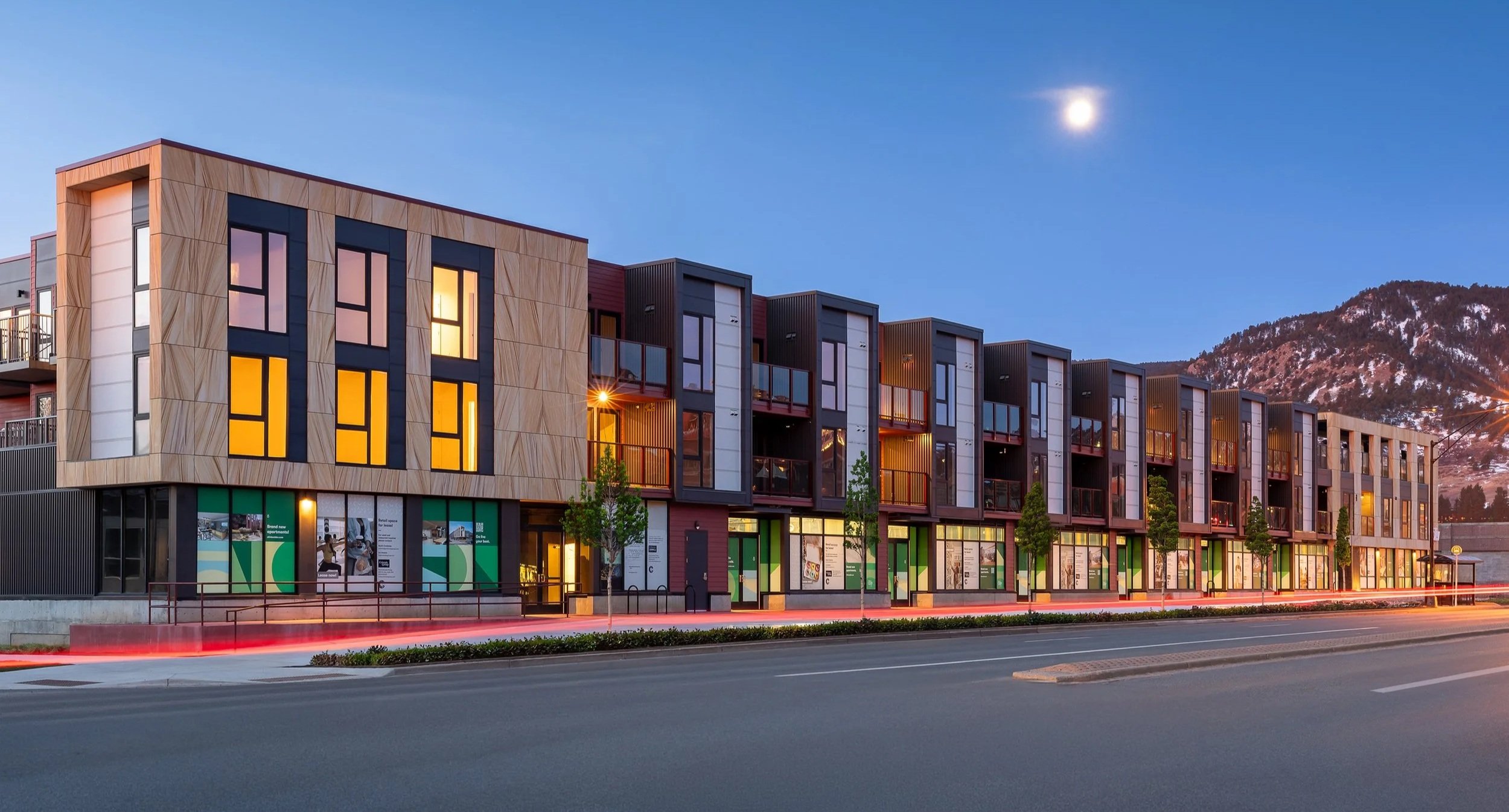 oLiv mixed-use development with modern apartments above ground-floor retail along a Boulder street at dusk with the Flatirons in the background. – Designed by Sopher Sparn Architects
