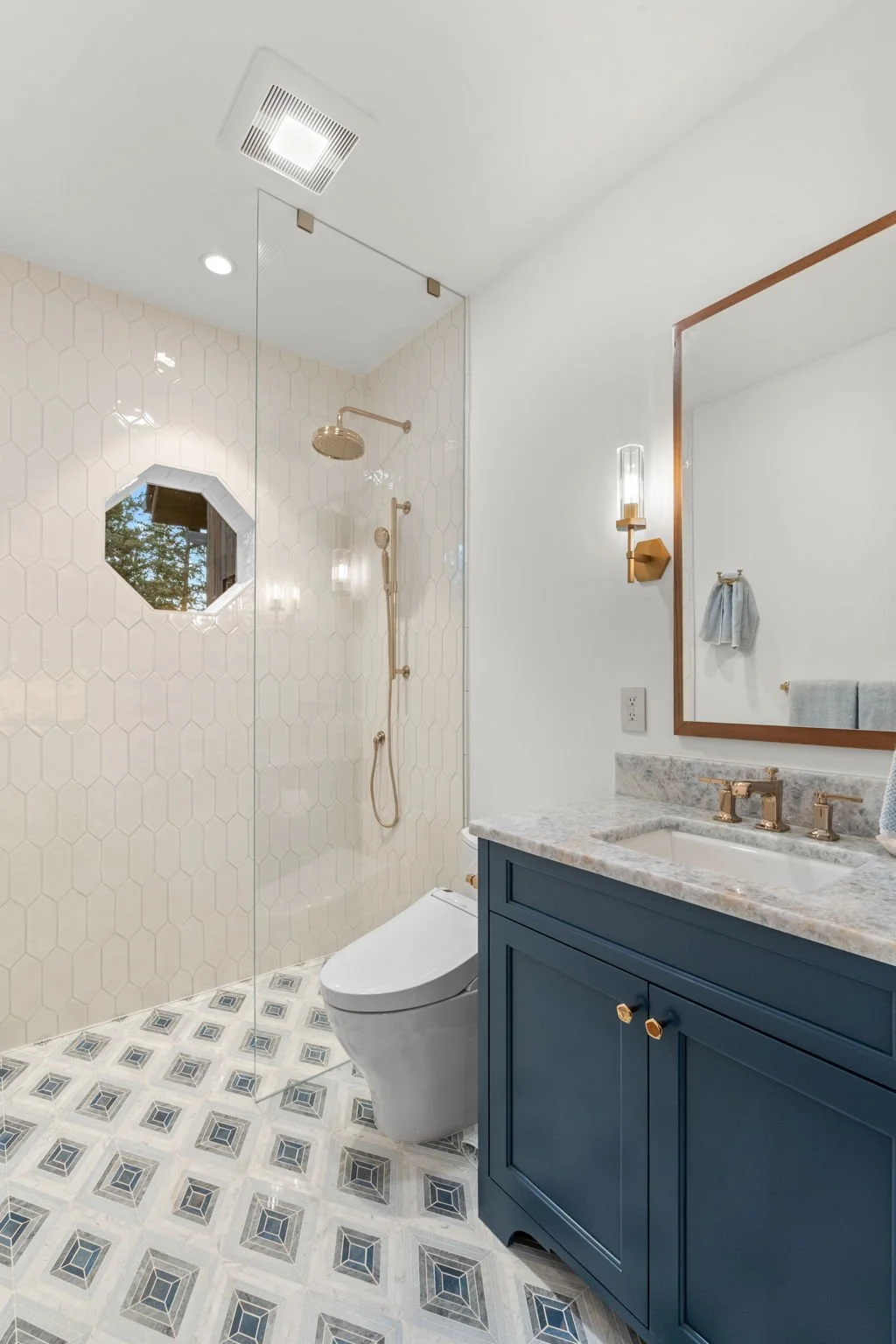 Bathroom at the Cedar & Stone residence in Jefferson County, Colorado, with blue vanity, marble countertop, hexagonal mirror, and walk-in shower.
