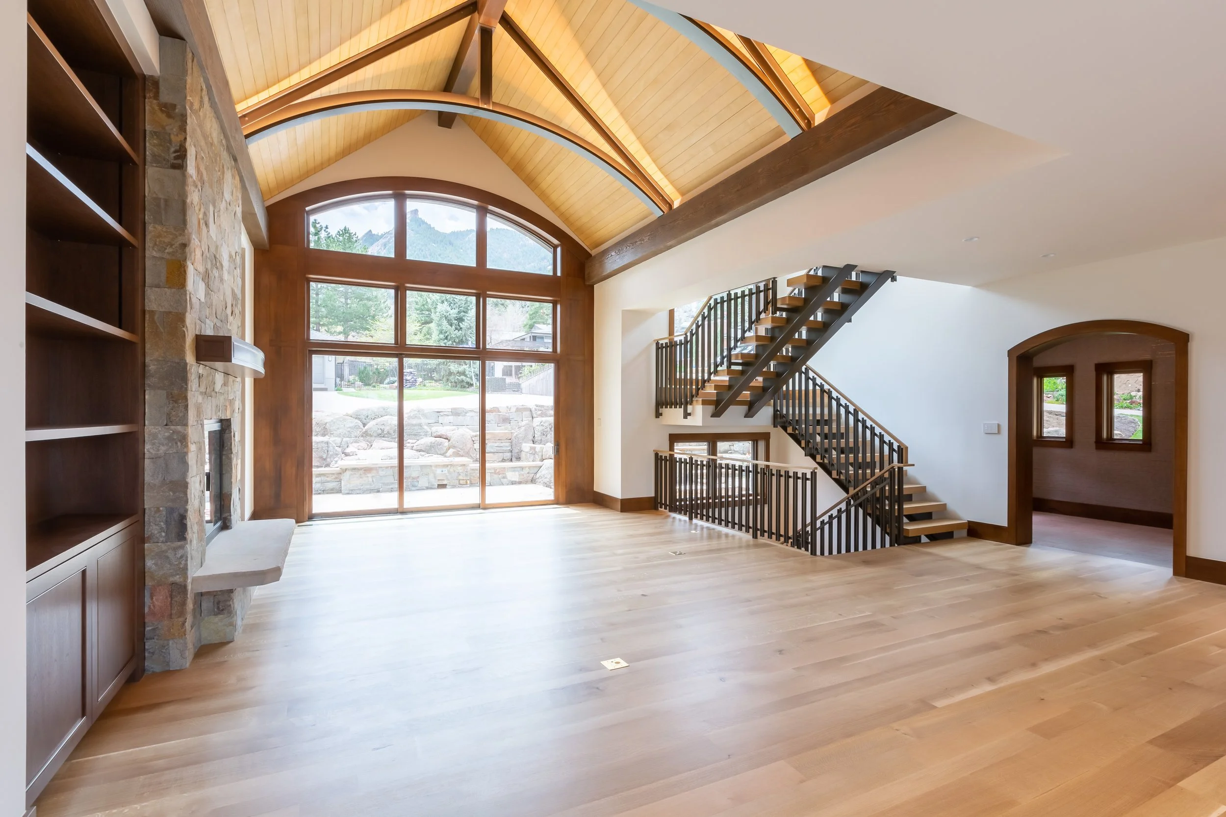Willowbrook, Boulder, CO – Bright living room with vaulted wooden ceiling, large windows, hardwood floors, built-in shelving, and staircase leading to the upper level.
