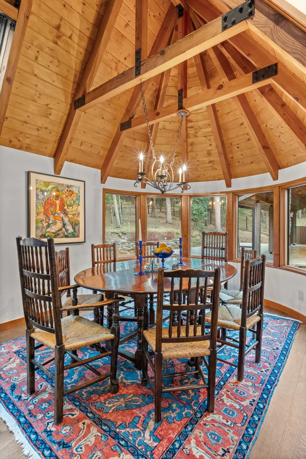 Dining room in the turret at the Cedar & Stone residence in Jefferson County, Colorado, with round wood table, vaulted wood ceiling, chandelier, and large window overlooking trees.
