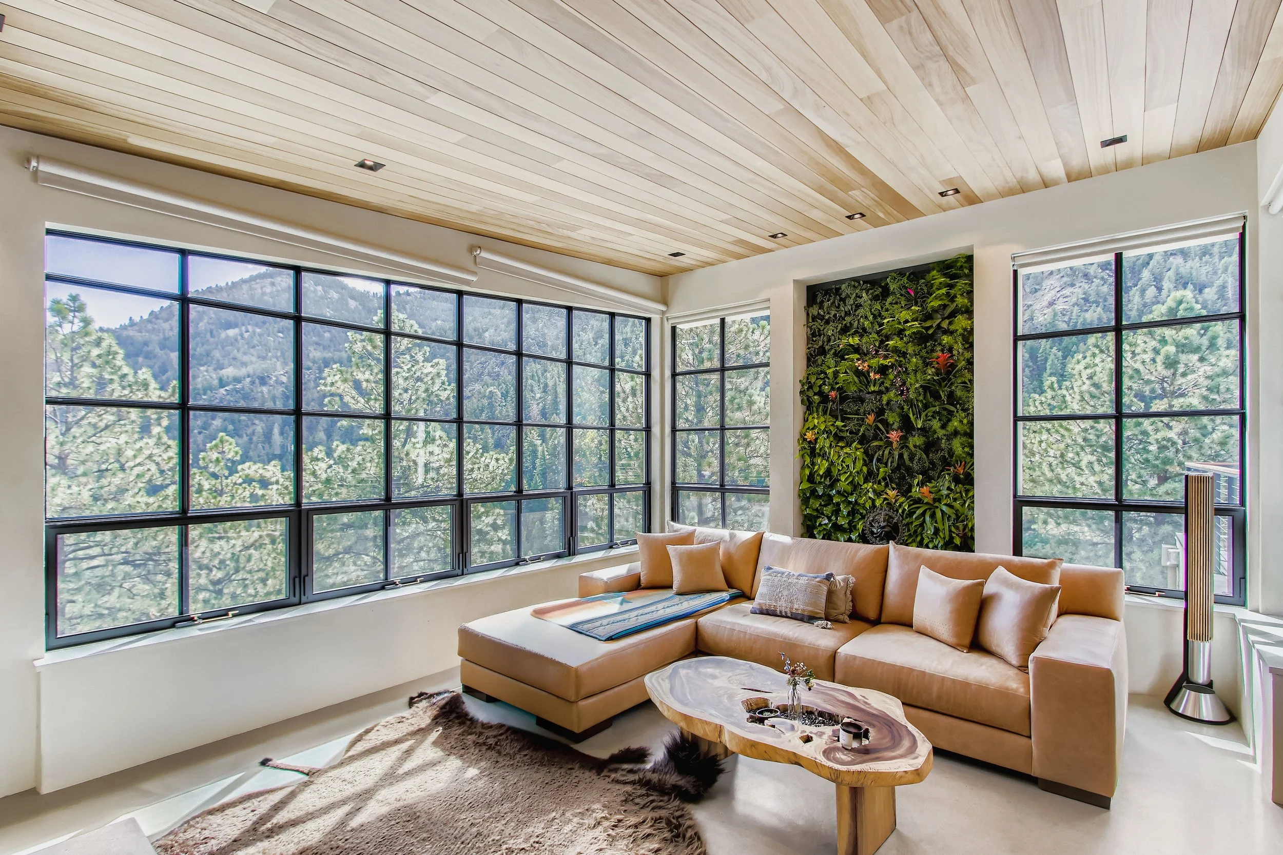 Living room in Onyx Ridge, Boulder County, CO, with large windows showing a mountain view, beige sectional sofa with pillows, wooden coffee table, and green wall decoration.
