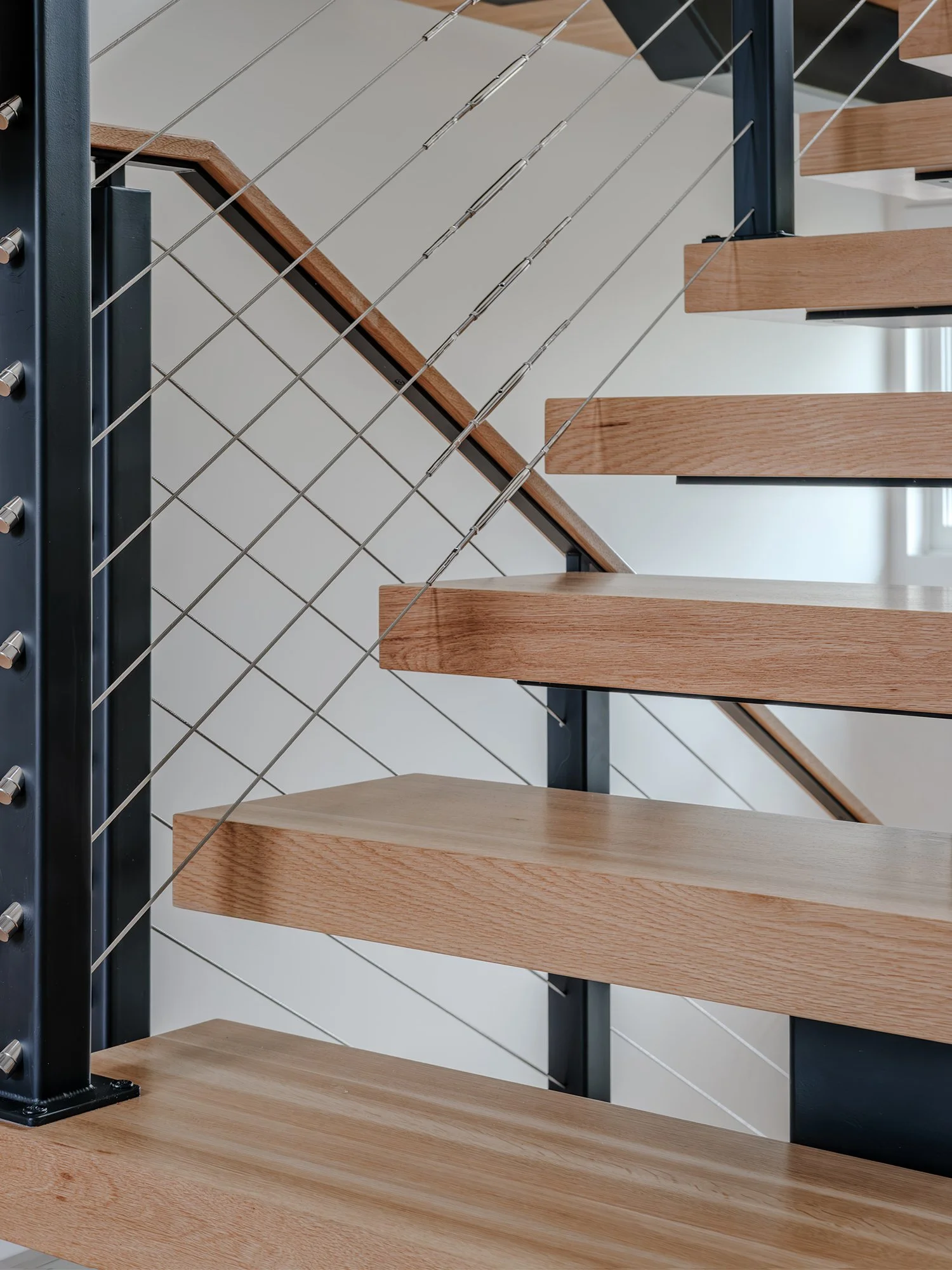 Close-up detail of floating wood stair treads with black metal railing and textured white wall finish.