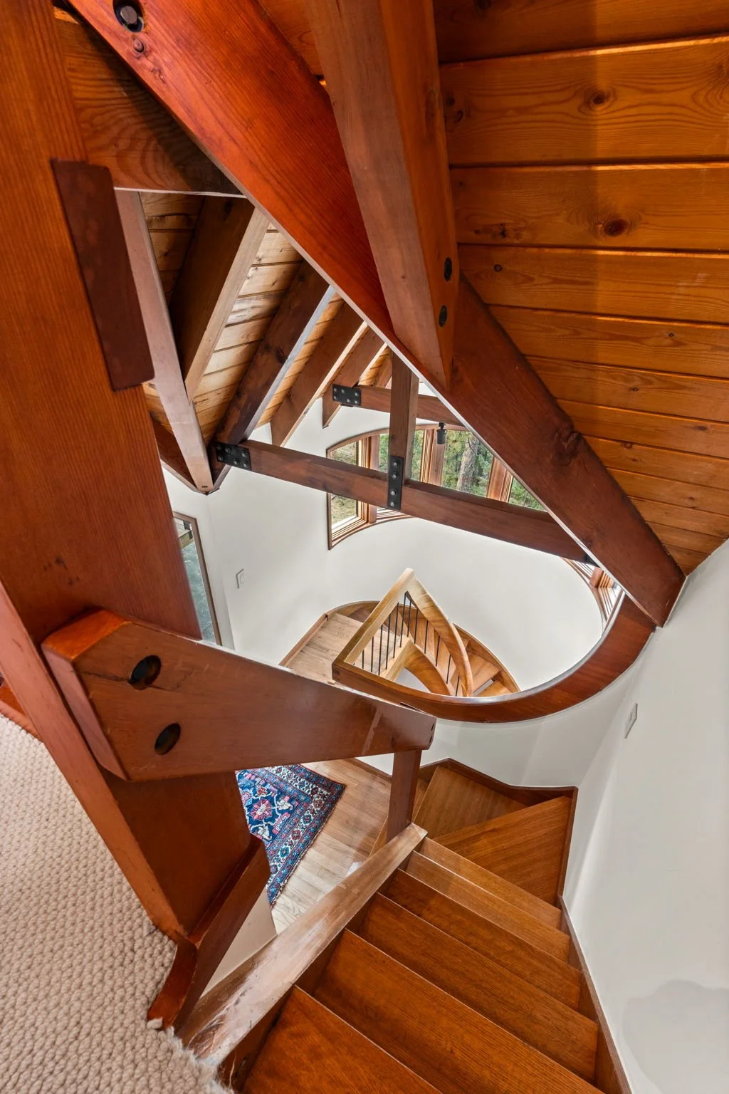 Curved staircase at the Cedar & Stone residence in Jefferson County, Colorado, with wood paneling and windows bringing in natural light.