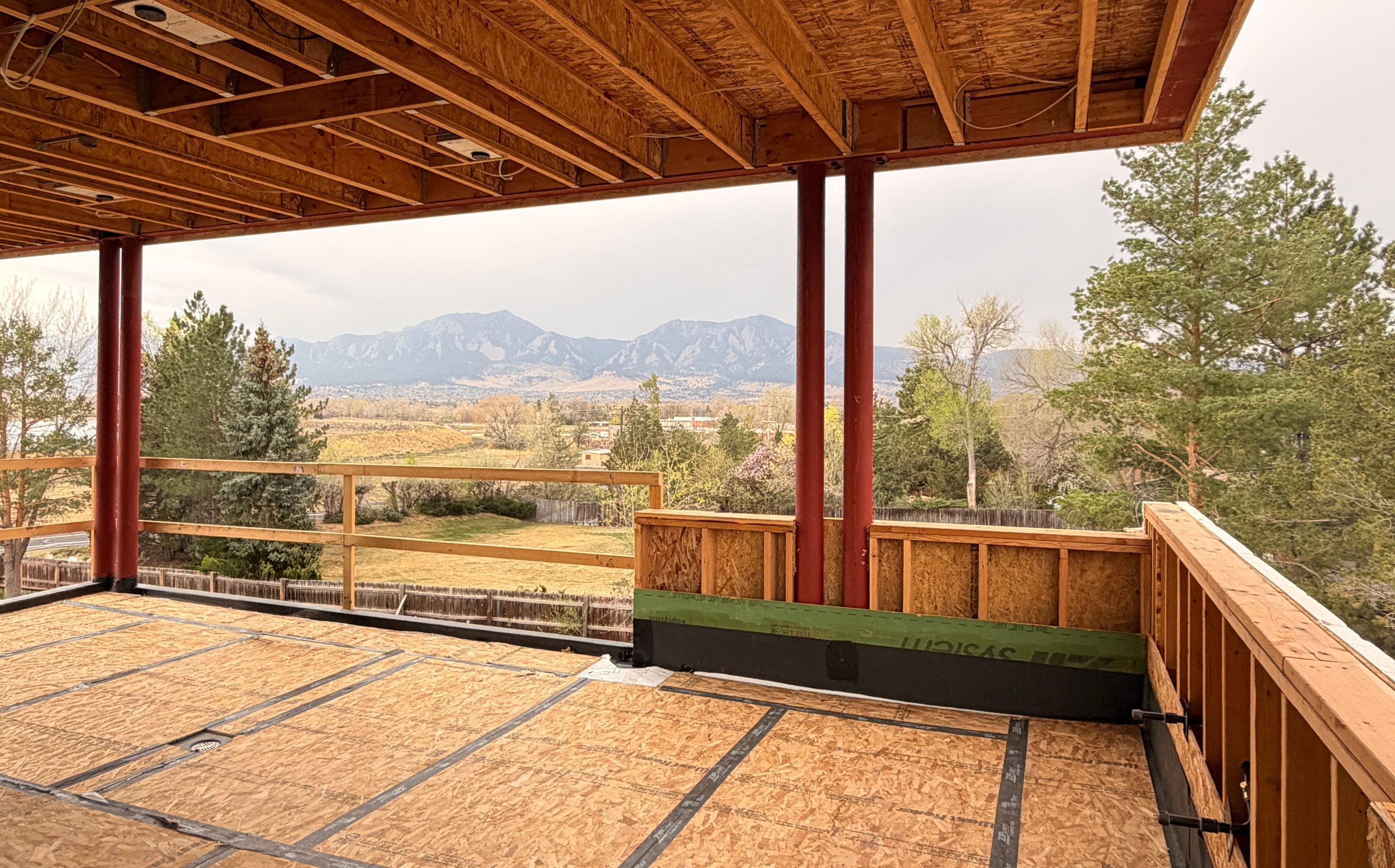 Covered outdoor terrace under construction with timber framing and panoramic views of the Boulder Flatirons and surrounding landscape. -Designed by Sopher Sparn Architects
