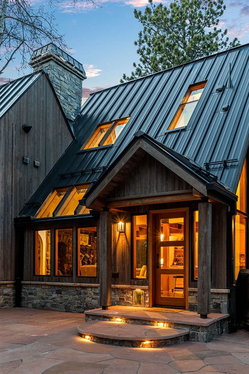 Cedar & Stone residence in Jefferson County, Colorado, featuring cedar siding, stone base, steep metal roof with skylights, and illuminated entry terrace.