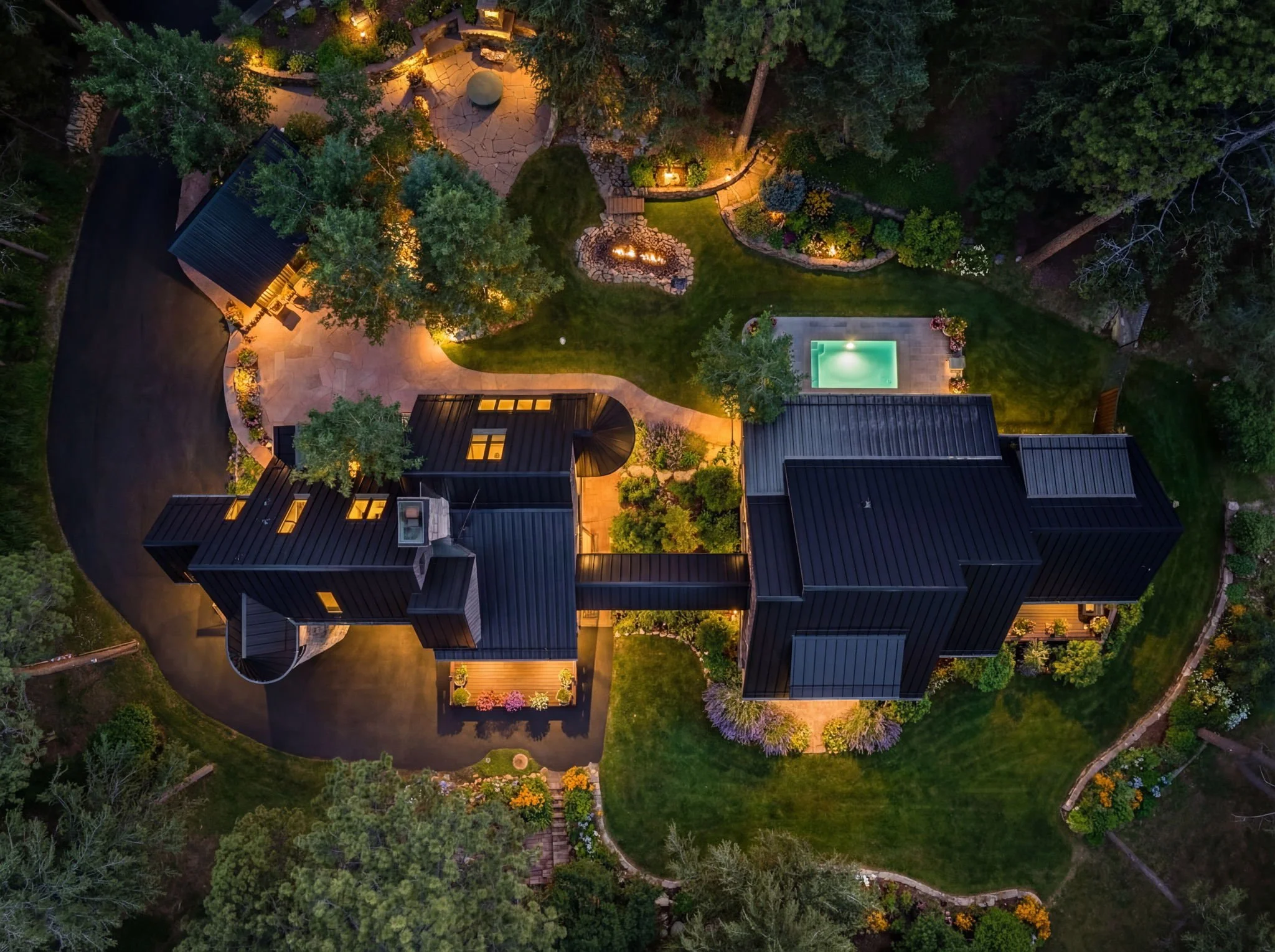 Aerial view of the Cedar & Stone residence in Jefferson County, Colorado, with metal roof, outdoor terraces, small pool, and landscaped gardens at night.