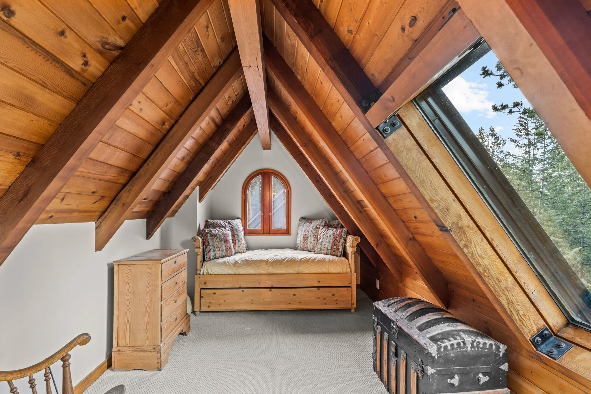 Bedroom at the Cedar & Stone residence in Jefferson County, Colorado, with exposed wood beams, skylights, and arched window overlooking trees.