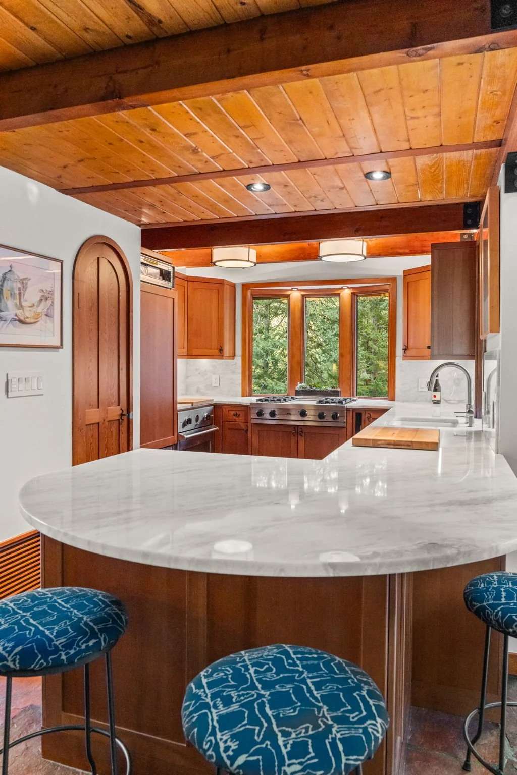 Kitchen at the Cedar & Stone residence in Jefferson County, Colorado, with wood cabinetry, marble island with seating, and large windows overlooking trees.