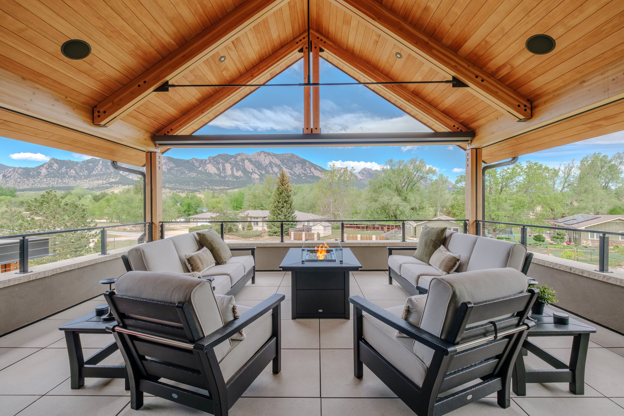 Covered outdoor living space with timber ceiling, lounge seating, fireplace, and expansive views of the flatirons. 