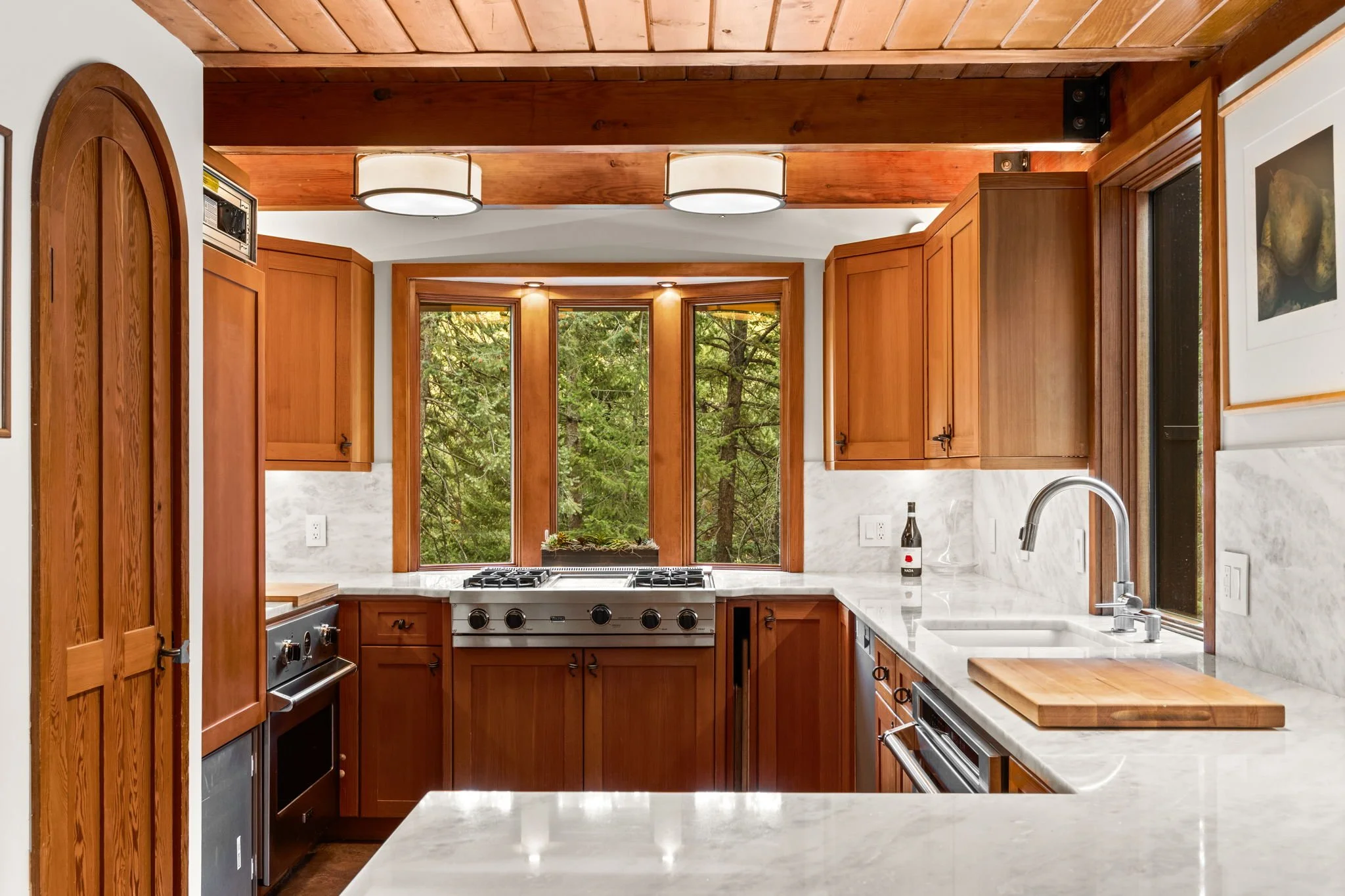 Kitchen at the Cedar & Stone residence in Jefferson County, Colorado, with wood cabinetry, marble countertops, and window views of surrounding trees.