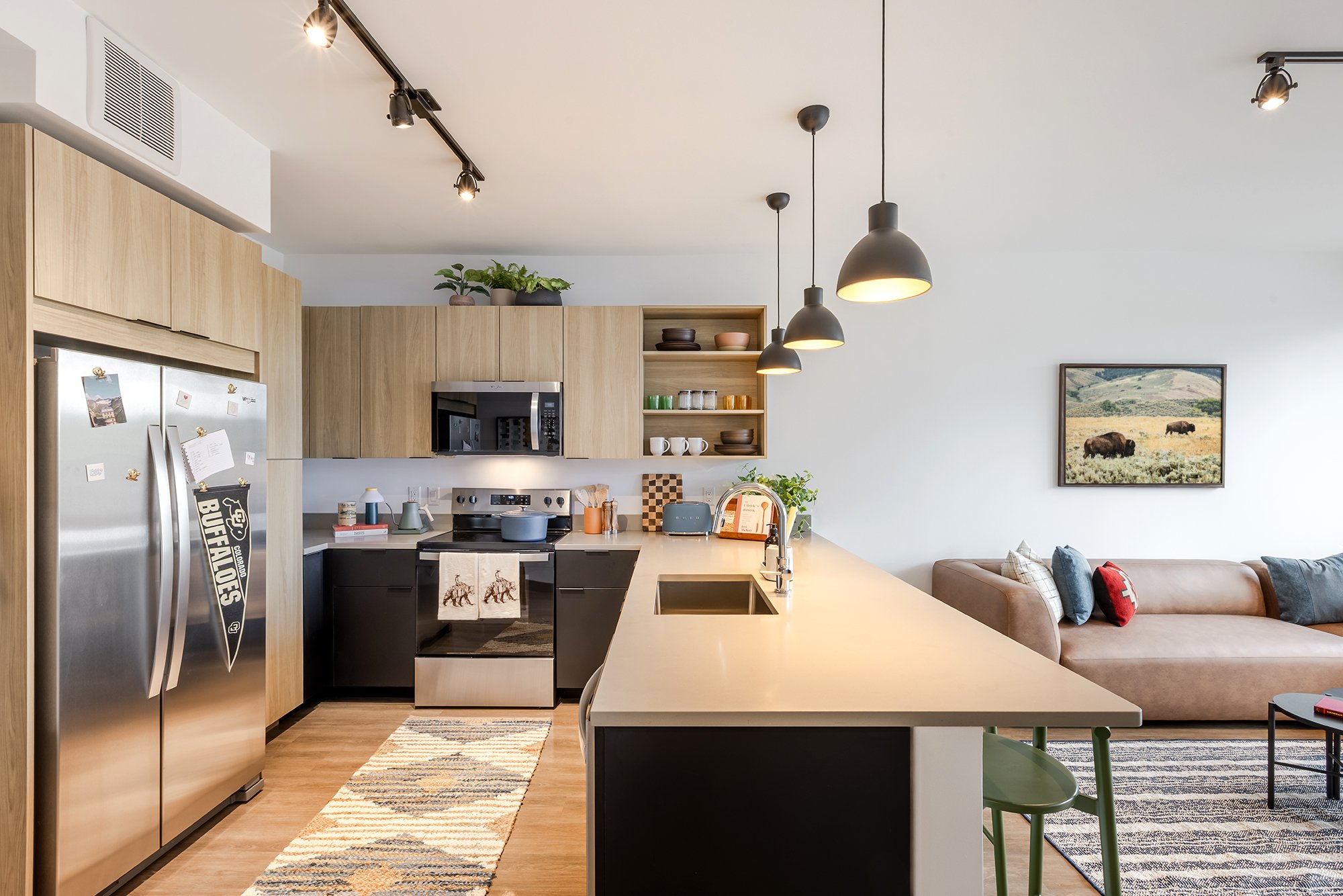 HUB 28th Street shared kitchen and living room featuring a large island, pendant lighting, open shelving, and contemporary finishes.
