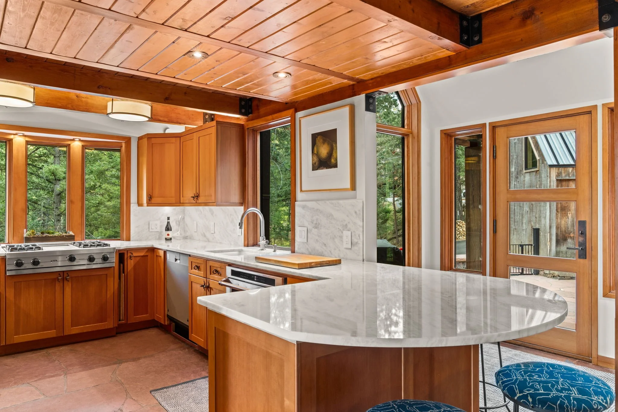 Kitchen at the Cedar & Stone residence in Jefferson County, Colorado, with wood cabinetry, marble countertops, and large windows overlooking the forest.