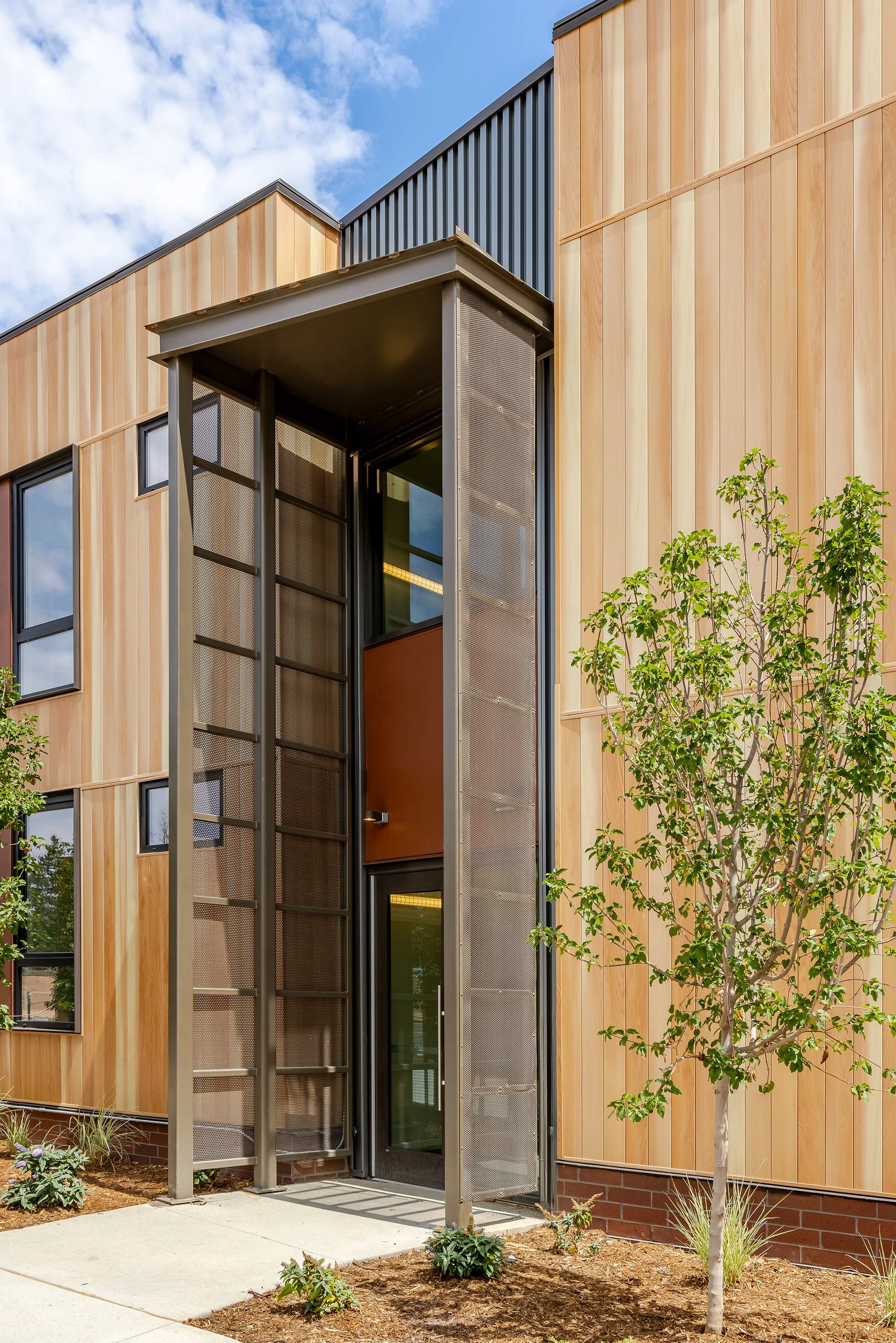 Detail of HUB 28th Street exterior showing vertical metal cladding, wood accents, windows, and climbing landscaping.