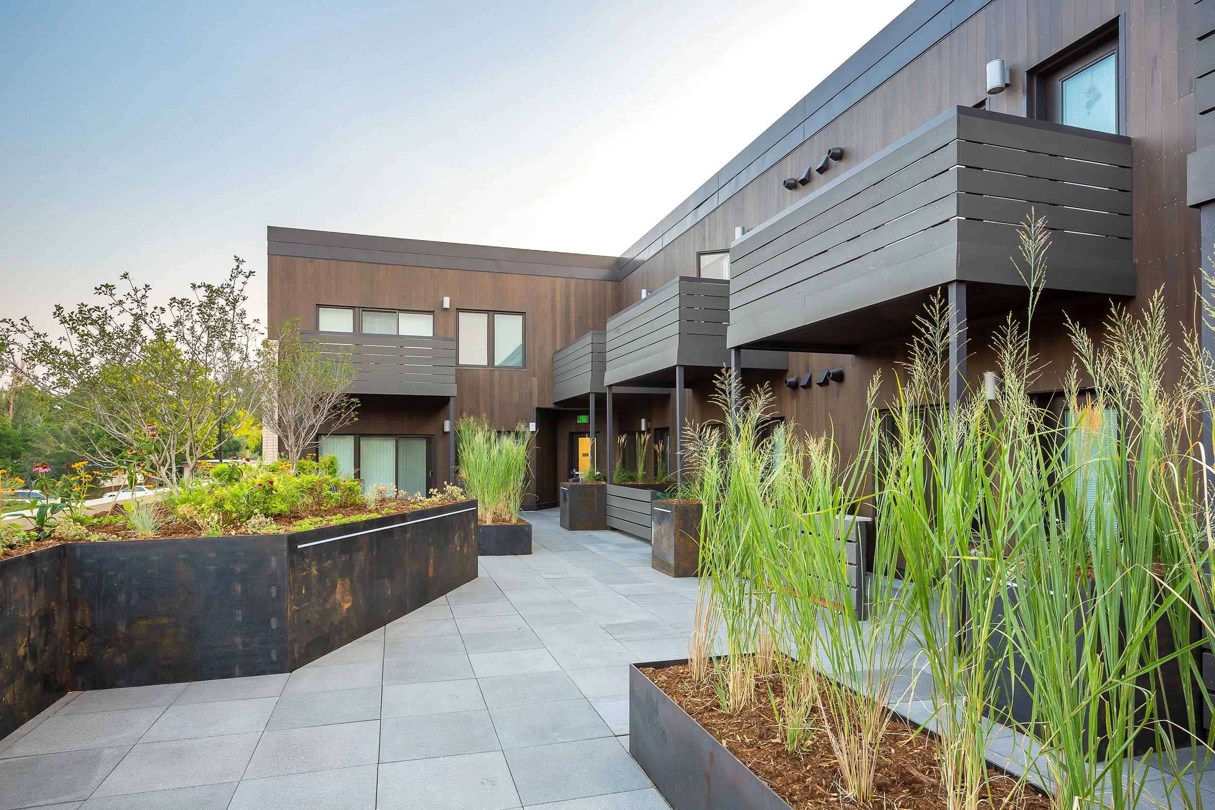 S’PARK Ciclo in Boulder, CO – Rooftop patio of a modern apartment building featuring potted plants, trees, and outdoor seating areas for residents.