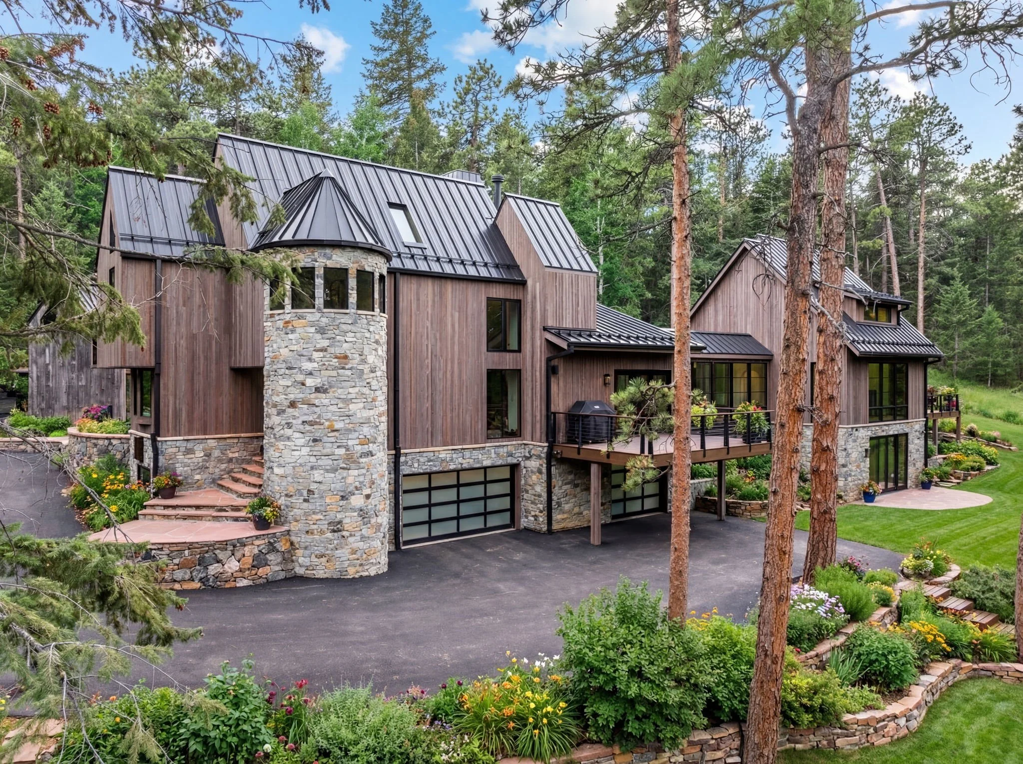 Cedar & Stone residence in Jefferson County, Colorado, featuring cedar siding, stone tower, standing-seam metal roof, and landscaped garden in wooded setting.