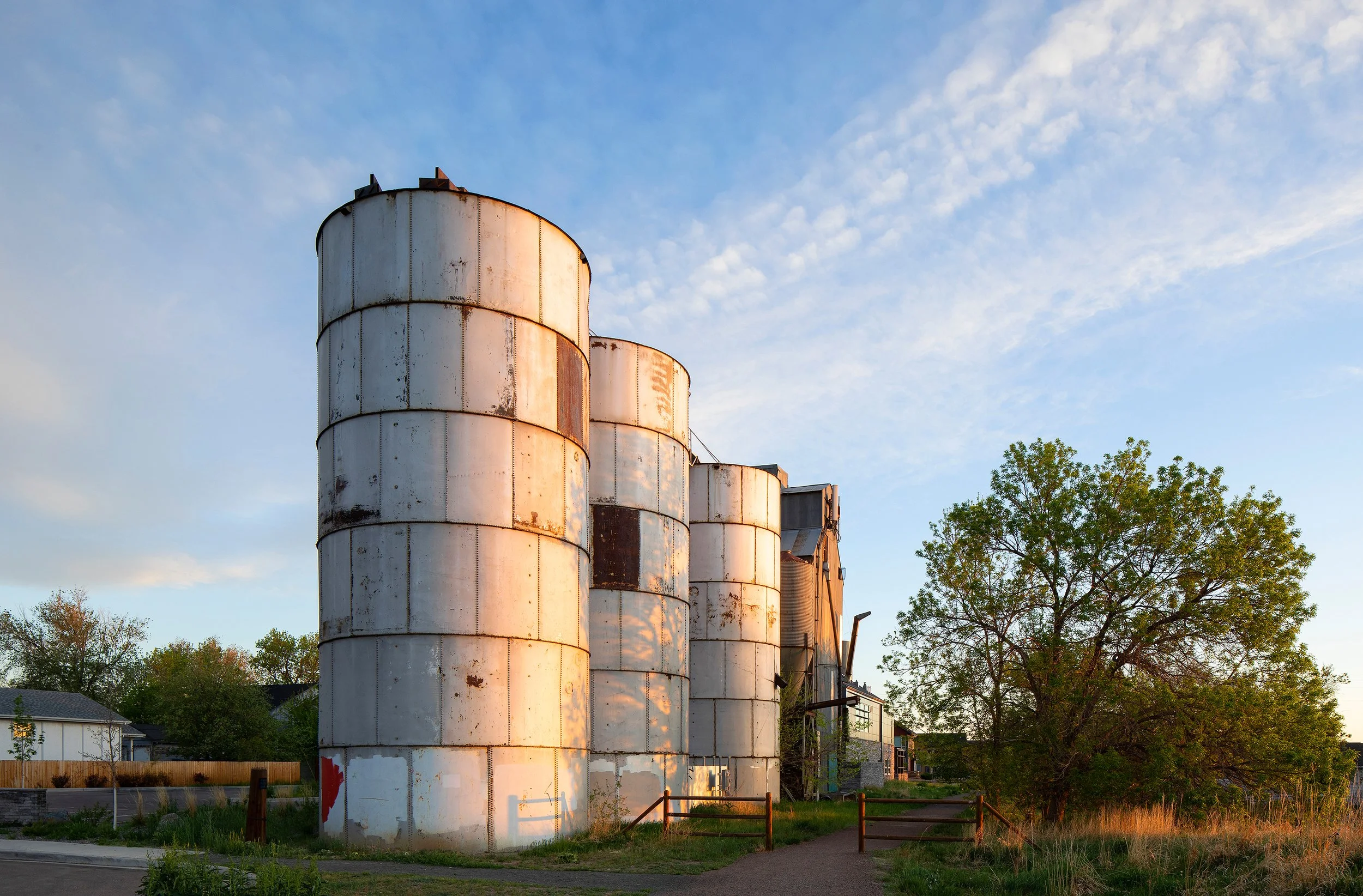 Historic silos adjacent to The Silos Wellness Center in Lafayette, CO, with clear blue sky and surrounding trees visible.