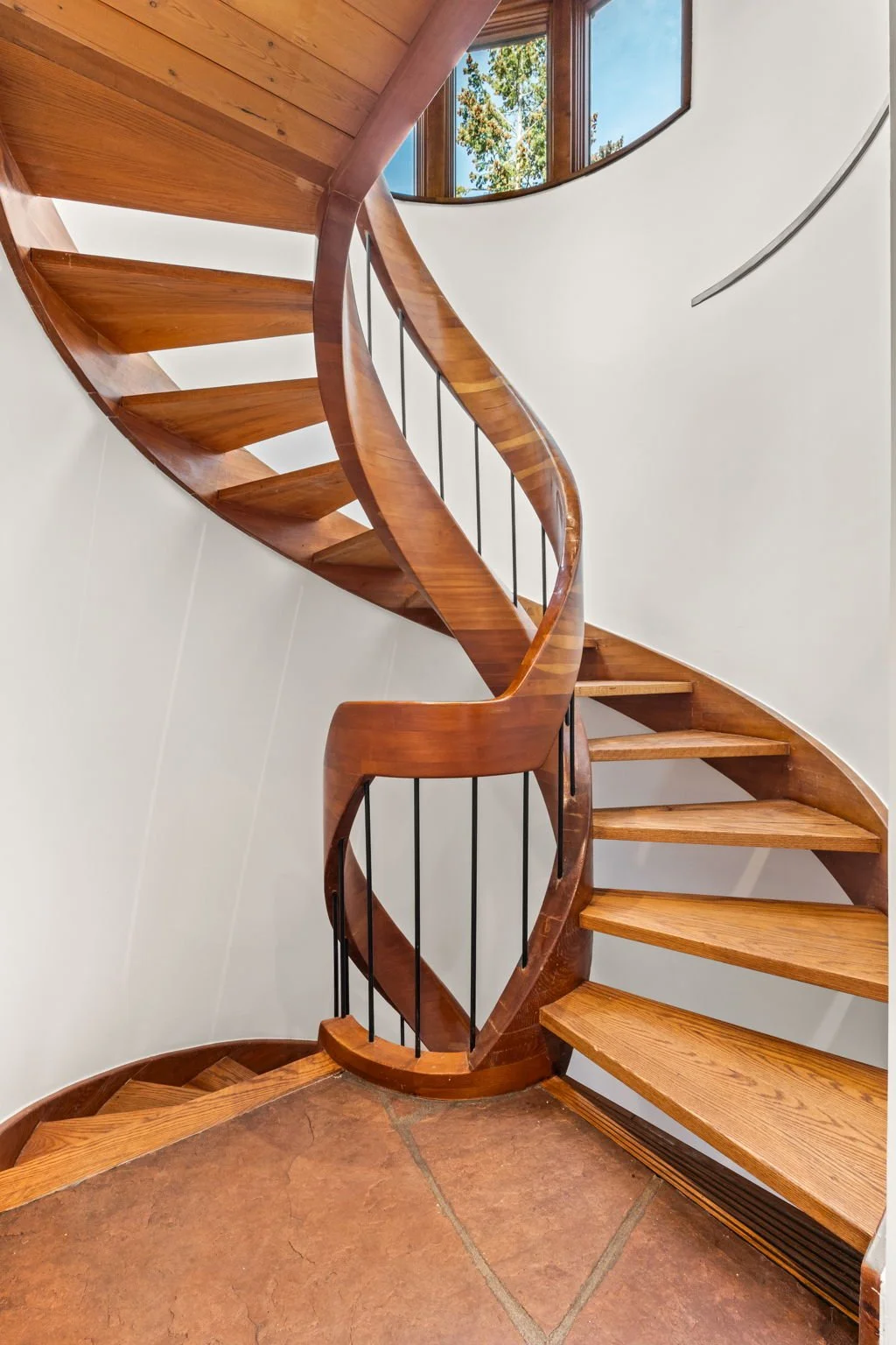 Spiral staircase at the Cedar & Stone residence in Jefferson County, Colorado, with wood steps, metal balusters, and window overlooking trees.