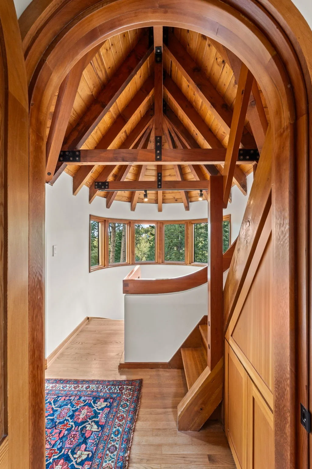 Interior corridor at the Cedar & Stone residence in Jefferson County, Colorado, with carved wood archway, exposed timber ceiling, and stair hall beyond.