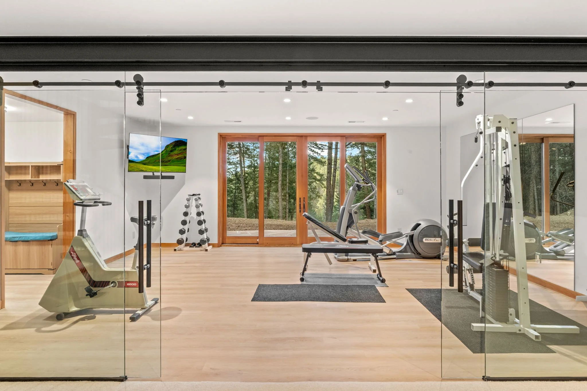 Home gym at the Cedar & Stone residence in Jefferson County, Colorado, with exercise equipment, wood accents, and large windows overlooking the forest.