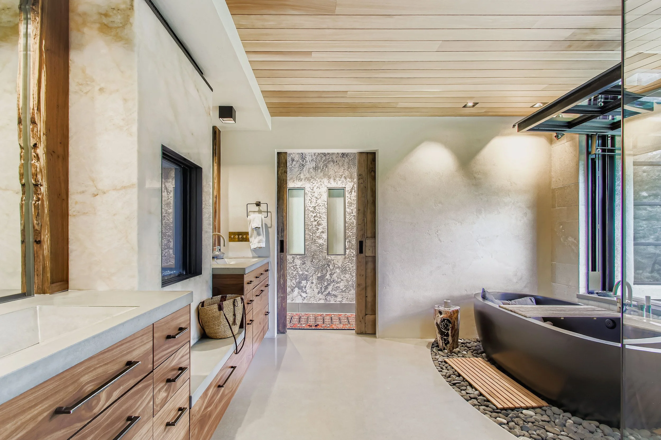 Bathroom at Onyx Ridge, Boulder County, CO, with wooden ceiling, sink cabinet, black freestanding bathtub on pebbled floor, and large window with natural light.