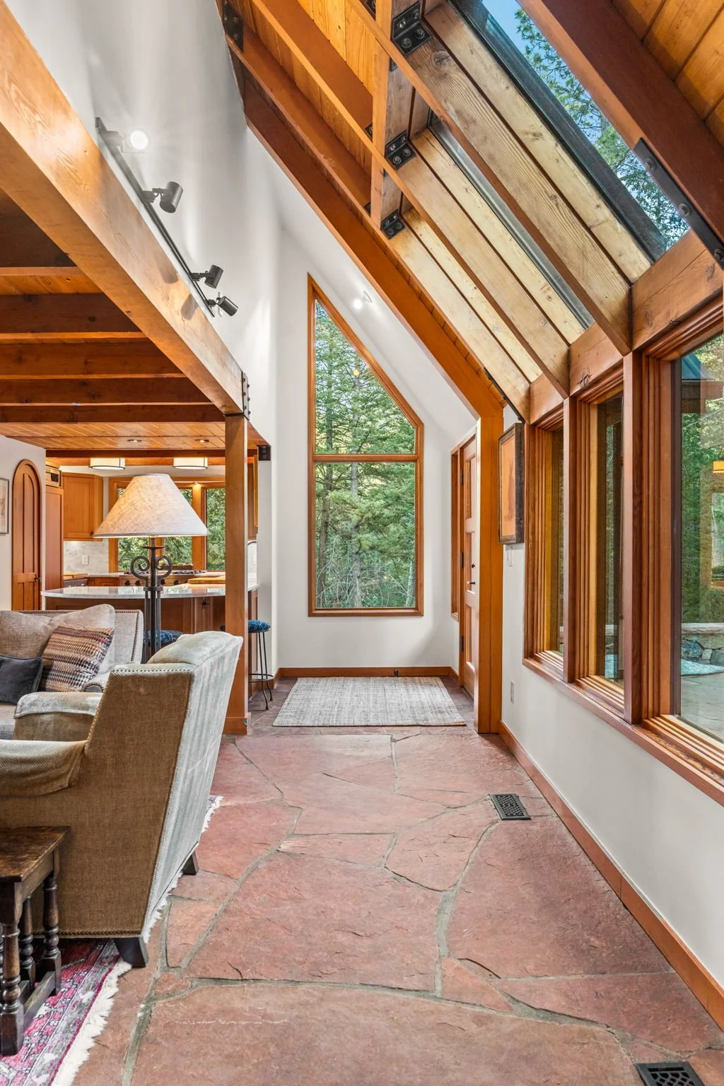 Living area at the Cedar & Stone residence in Jefferson County, Colorado, with wood-framed windows, sloped glass ceiling, and views of the surrounding forest.