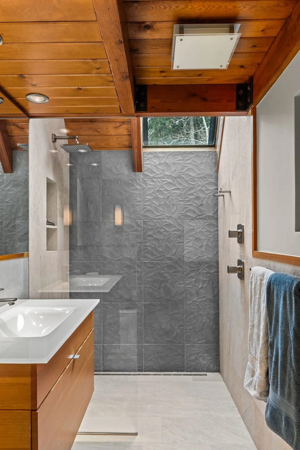 Bathroom at the Cedar & Stone residence in Jefferson County, Colorado, with walk-in shower, textured gray tile, wood ceiling, and window overlooking trees.