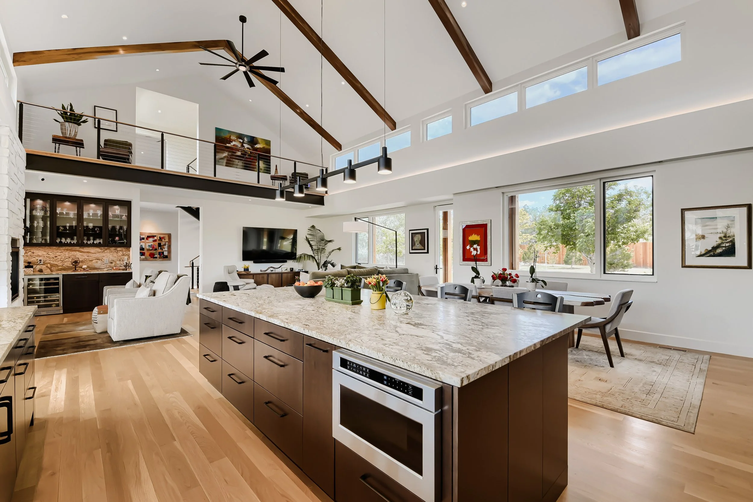 Contemporary kitchen with dark custom cabinetry, stone countertops, exposed beams, and floor-to-ceiling windows framing mountain views.