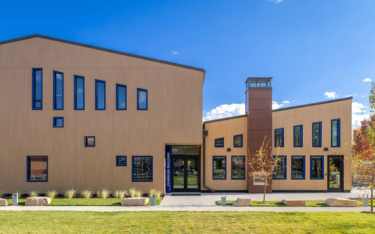 Exterior view of Boulder Country Day School Commons Building, tan facade with large windows, entryway, and landscaped grounds.