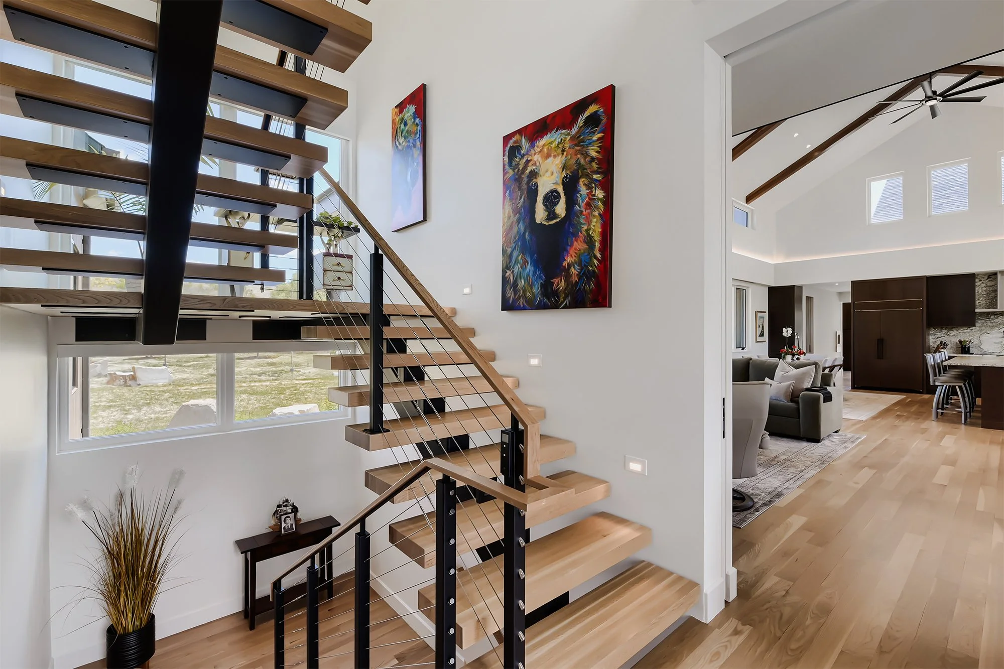 Open wood staircase with black metal railing, modern artwork, and exposed beam ceiling details.