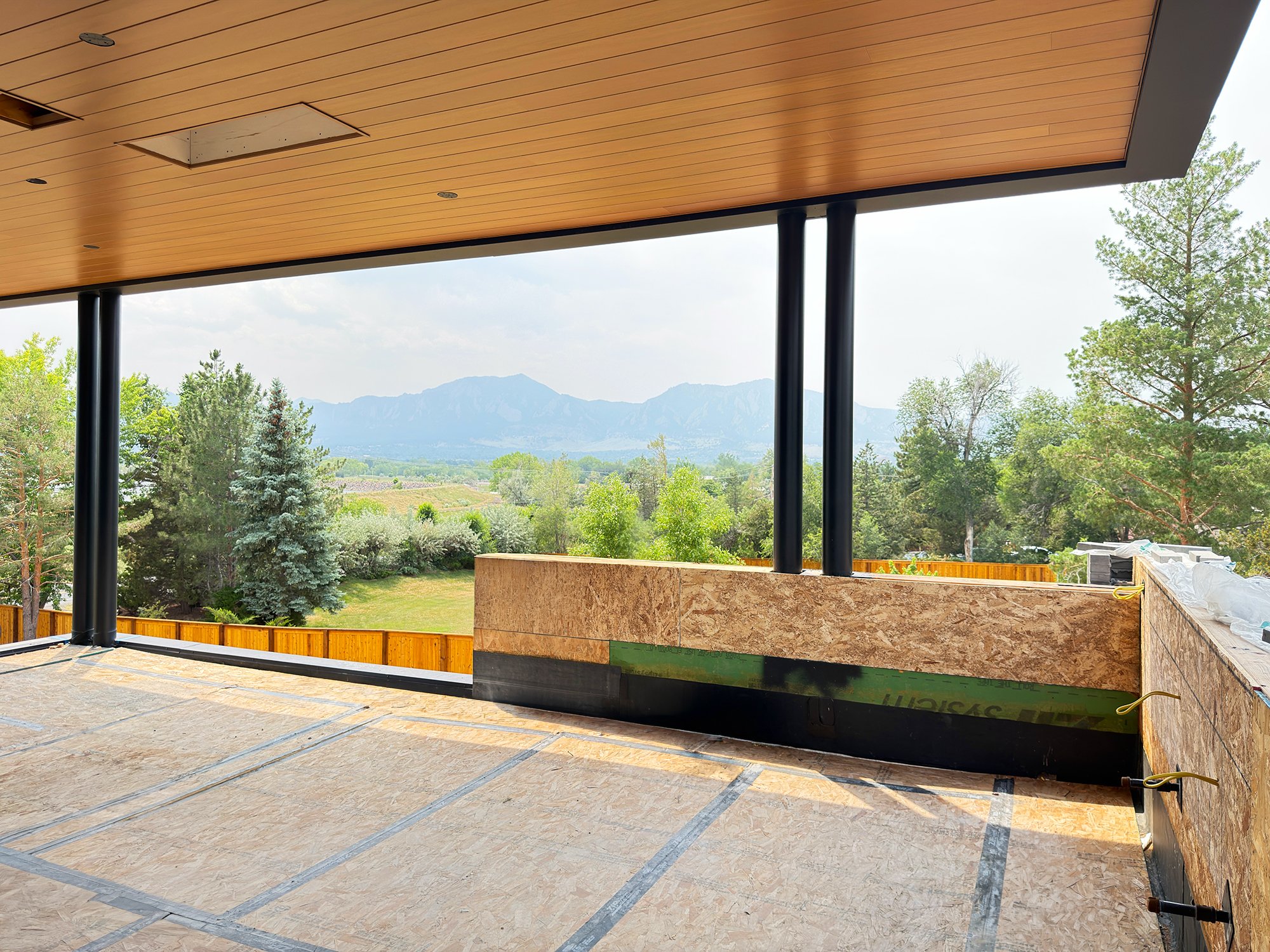 Covered outdoor terrace under construction with timber framing and panoramic views of the Boulder Flatirons and surrounding landscape. -Designed by Sopher Sparn Architects