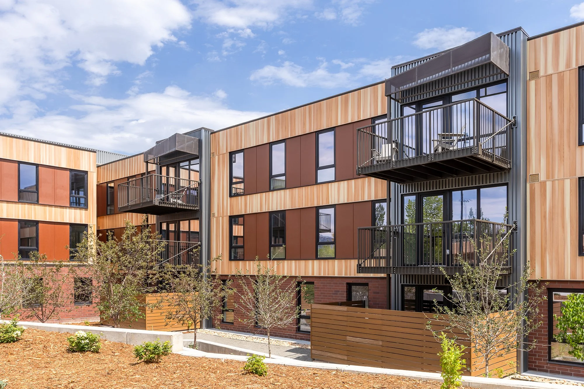 HUB 28th Street residential facade featuring brick, dark metal balconies, large windows, and native landscaping.