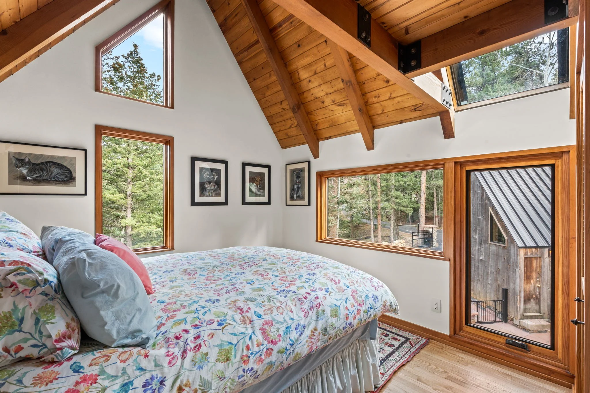 Bedroom at the Cedar & Stone residence in Jefferson County, Colorado, with wood ceiling, large windows, and views of the surrounding forest.
