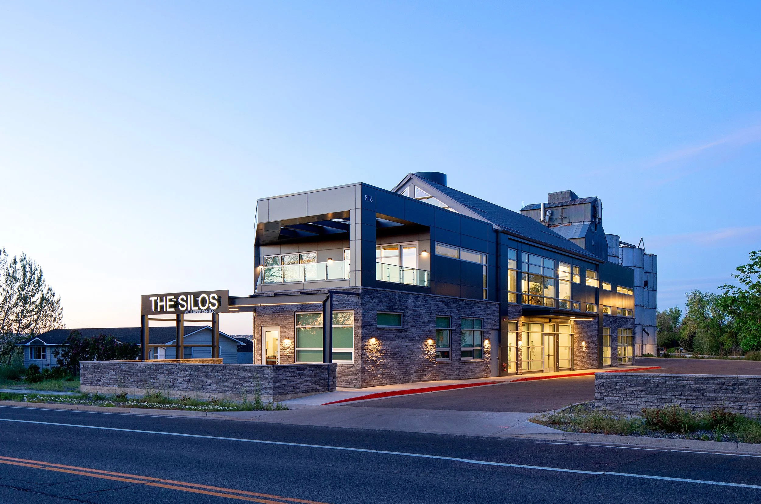Exterior view of The Silos Wellness Center in Lafayette, CO, showing the modern building with metal, glass, and stone elements at dusk.