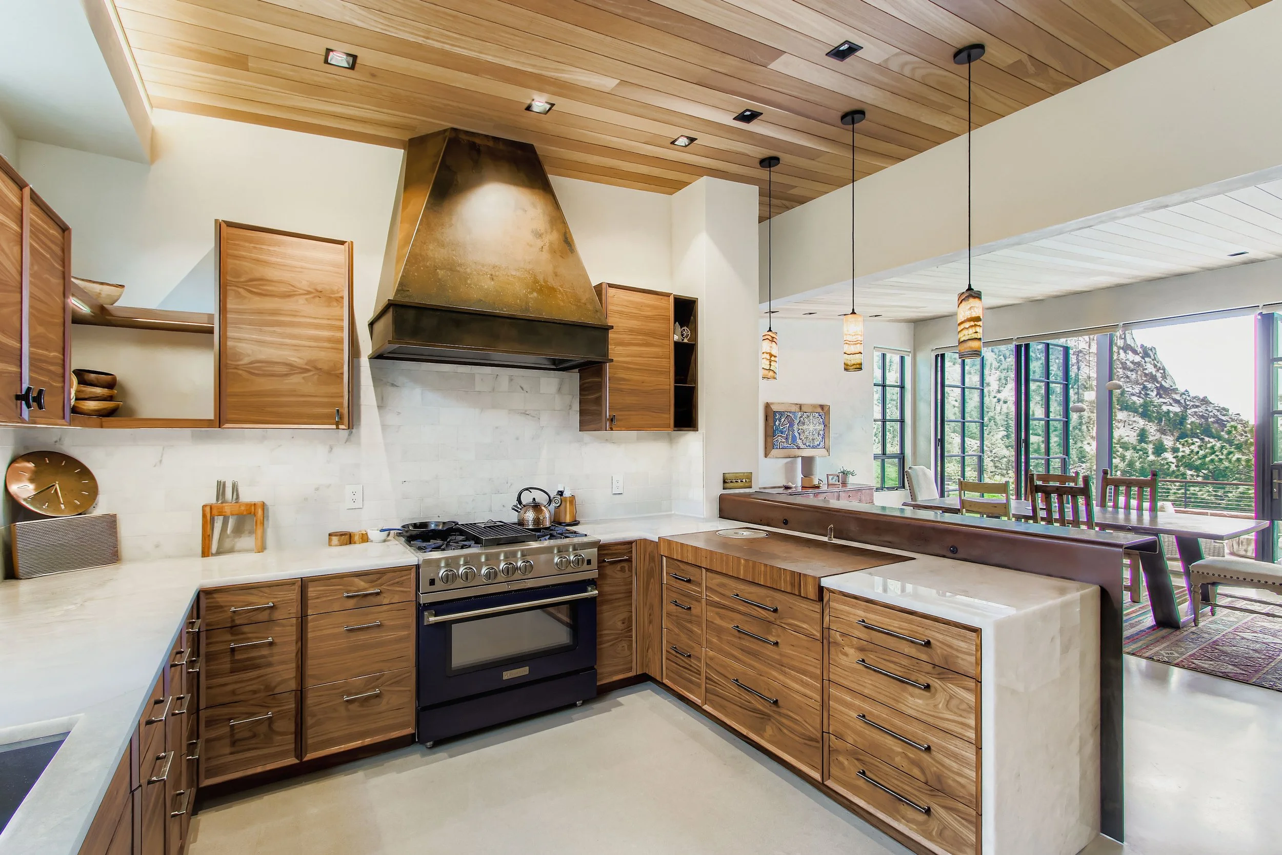 Kitchen in Onyx Ridge, Boulder County, CO, featuring wooden cabinets, marble countertops, stainless steel oven, and an open view into the dining area with floor-to-ceiling windows showcasing mountain scenery.
 – Designed by Sopher Sparn Architects LL