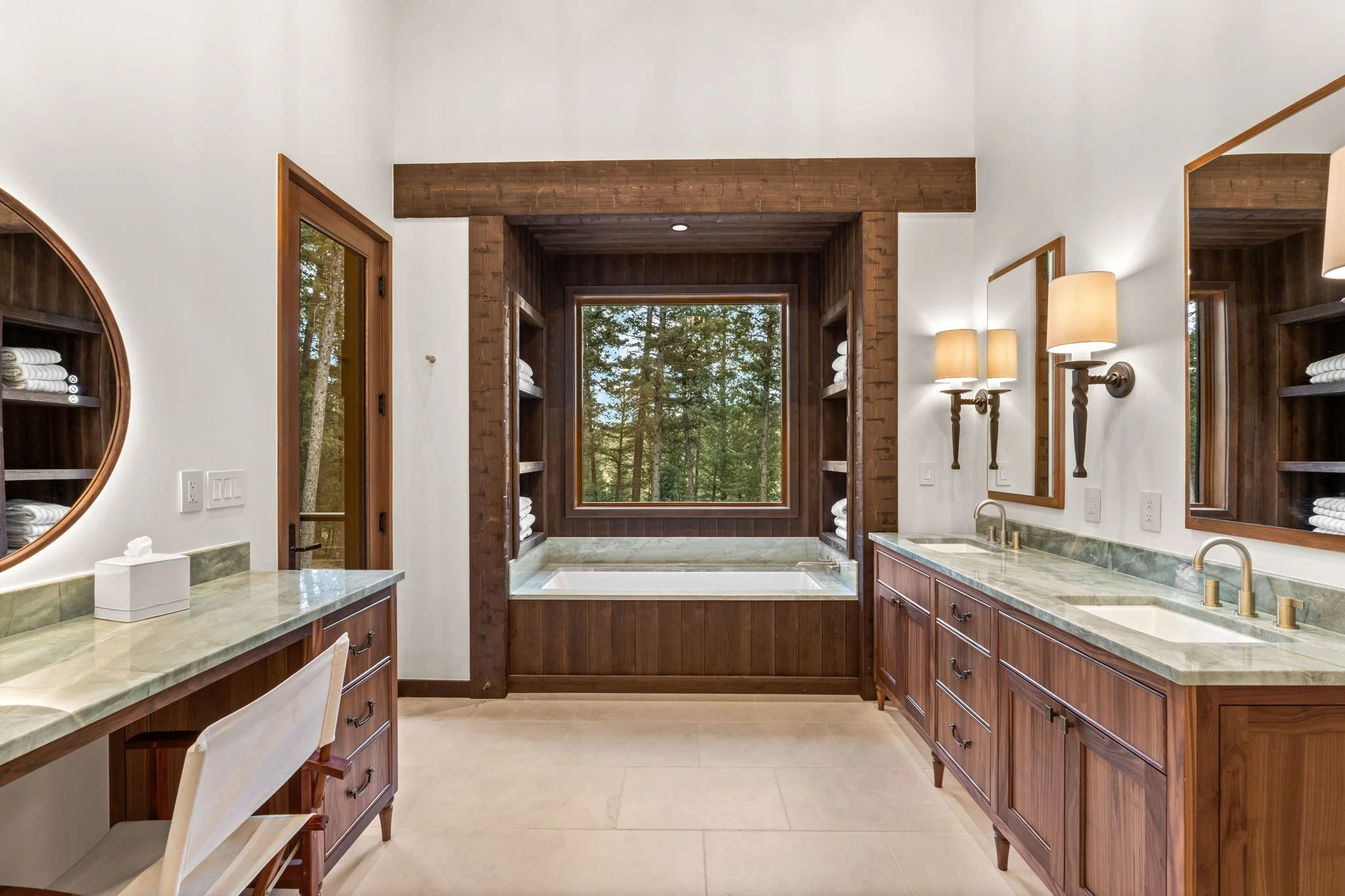 Bathroom at the Cedar & Stone residence in Jefferson County, Colorado, with double vanity, marble countertop, wood cabinetry, and bathtub beneath a window overlooking trees.