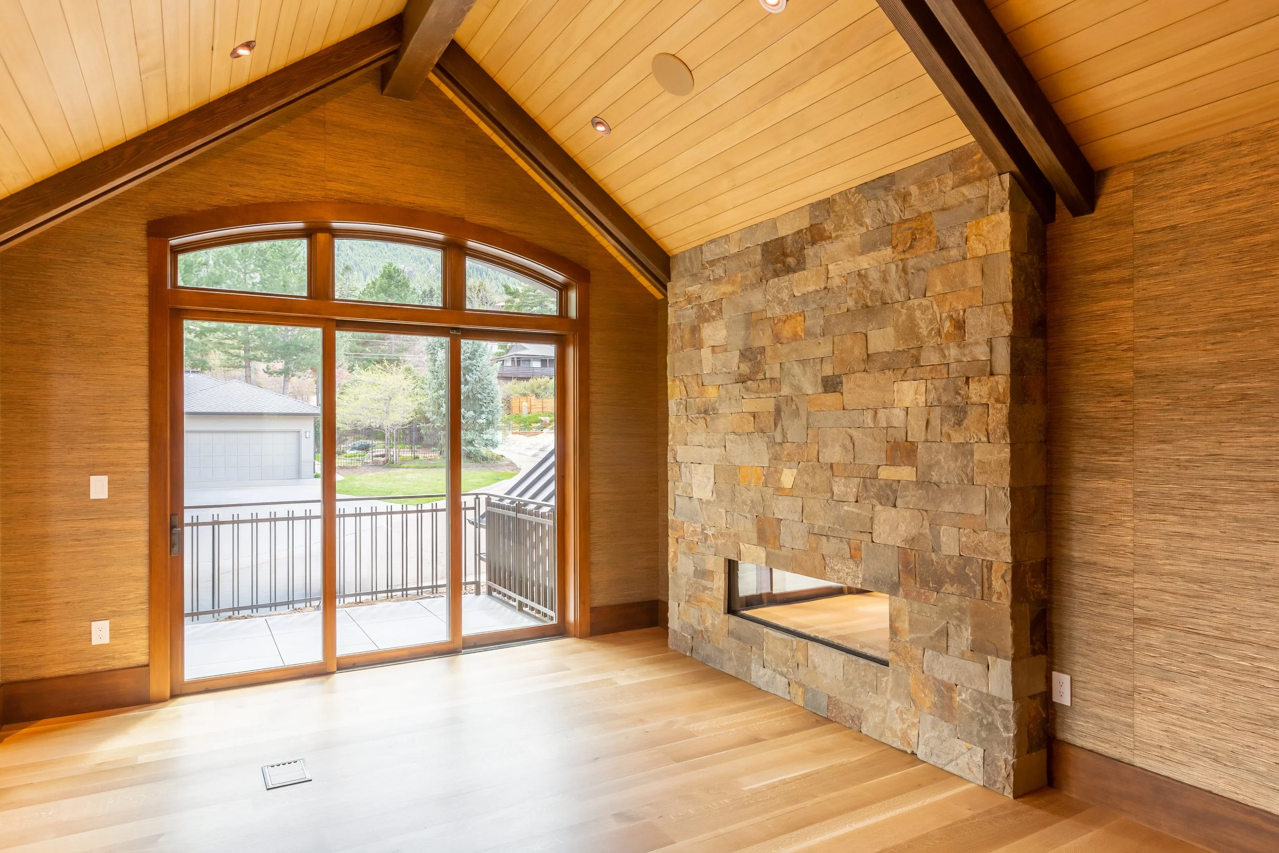 Elegant living room at Willowbrook in Boulder, CO, with wooden floors, stone fireplace, and large sliding glass door leading to a balcony with views of the surrounding neighborhood.