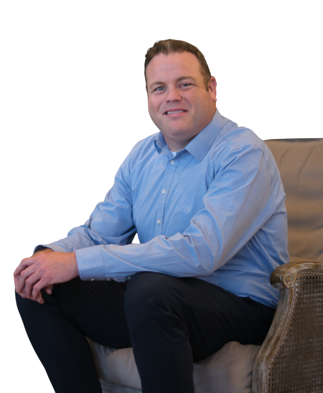 A man smiling outdoors in front of trees, wearing a blue jacket over a collared shirt.