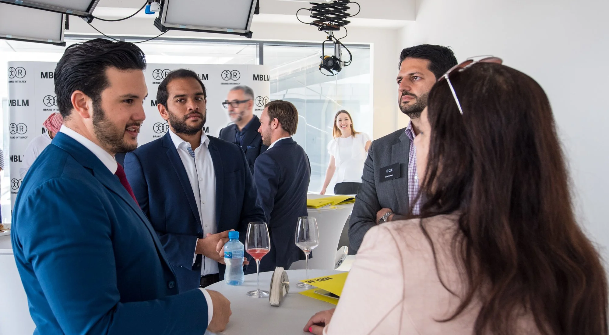A group of well-dressed professionals engaging in conversation at a networking event or corporate gathering in a modern, bright conference room.