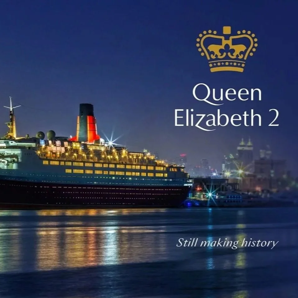 Nighttime photo of the Queen Elizabeth 2 cruise ship docked at a harbor, with city skyline in the background. Graphic overlay includes a gold crown, and the text 'Queen Elizabeth 2' with the slogan 'Still making history'.