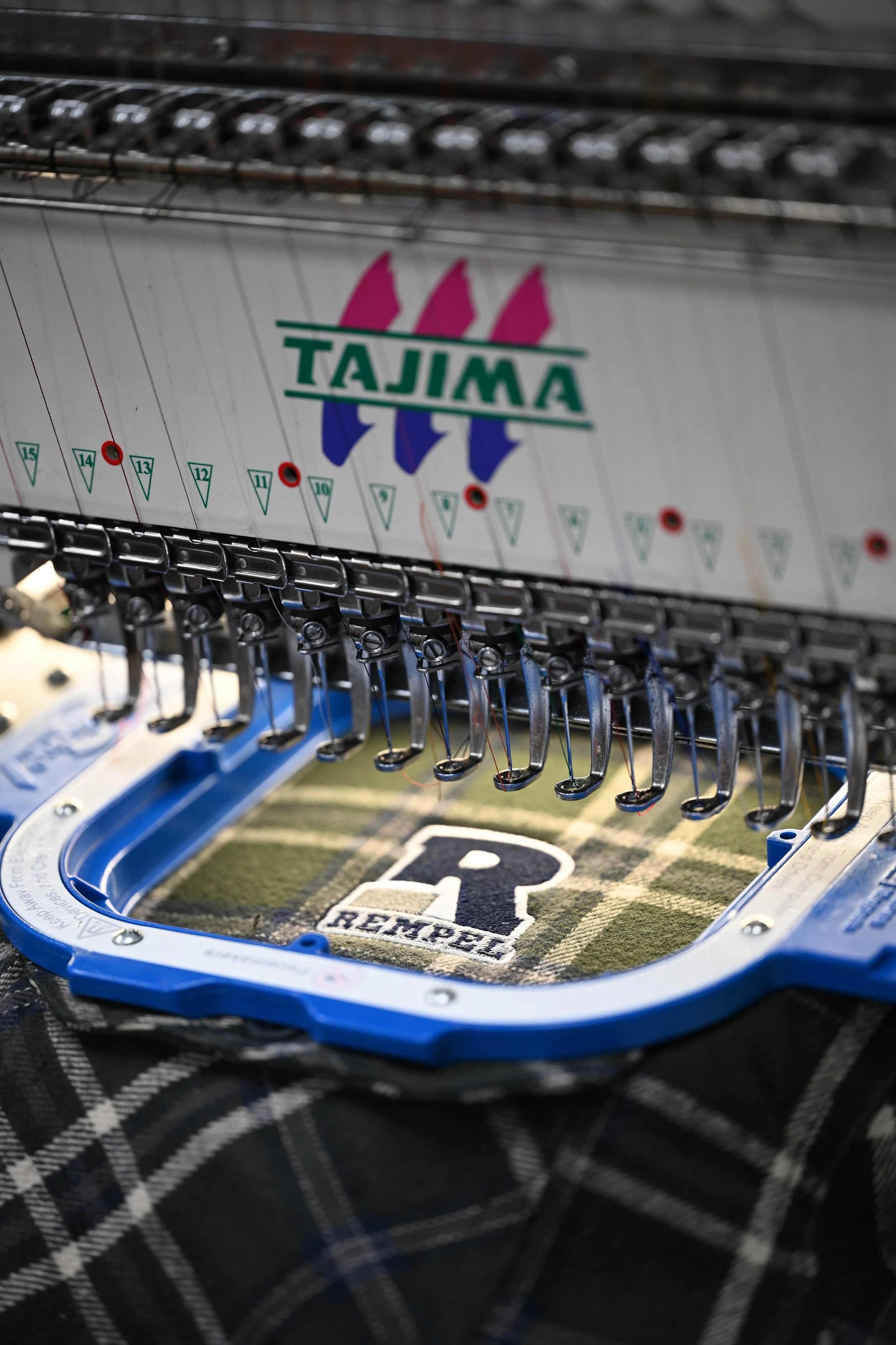 An Embroidery machine printing out a logo design onto a flannel shirt.