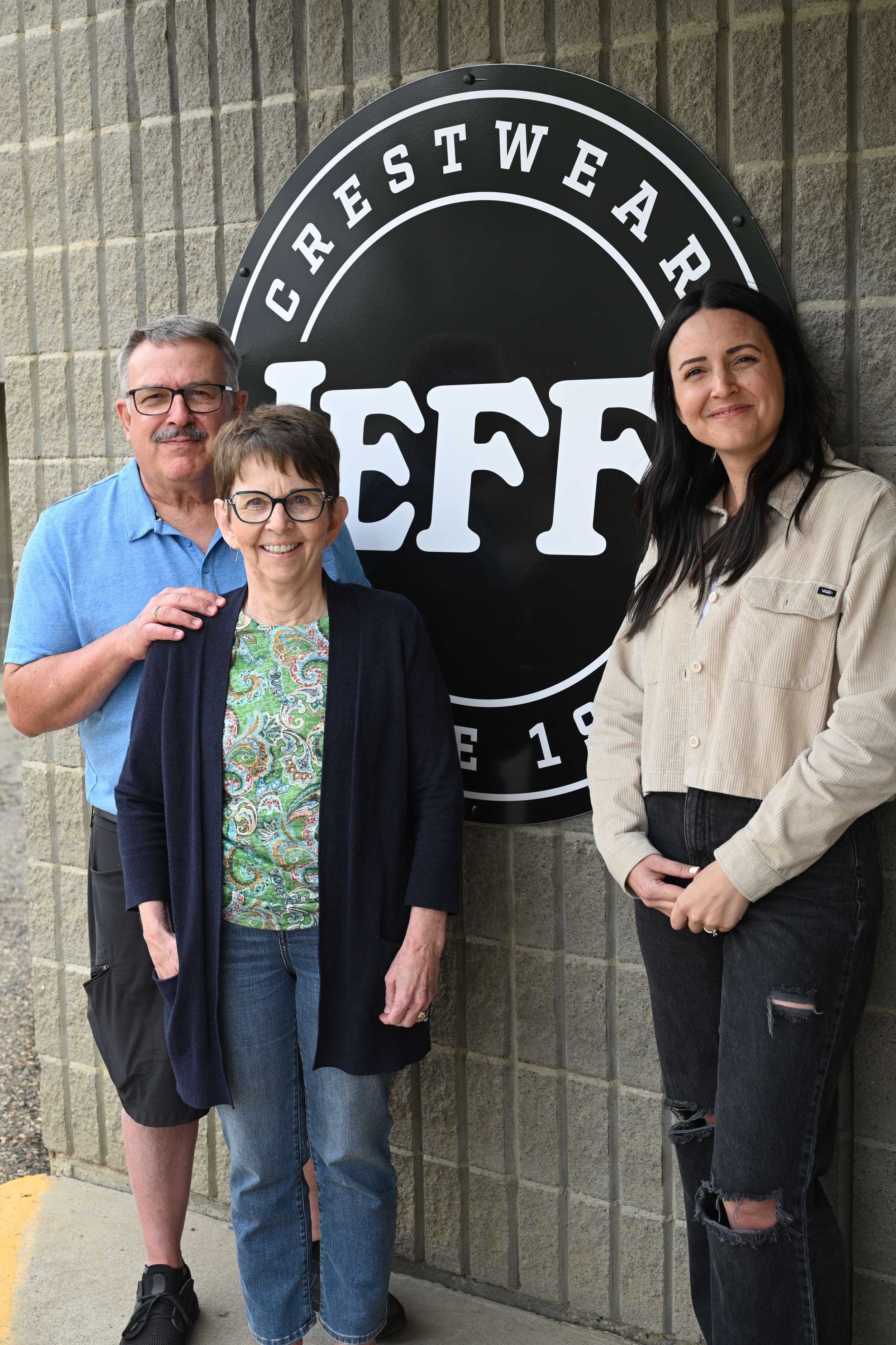 Three people standing in front of a restaurant sign that reads 'CRESTWEAR TEFF'.