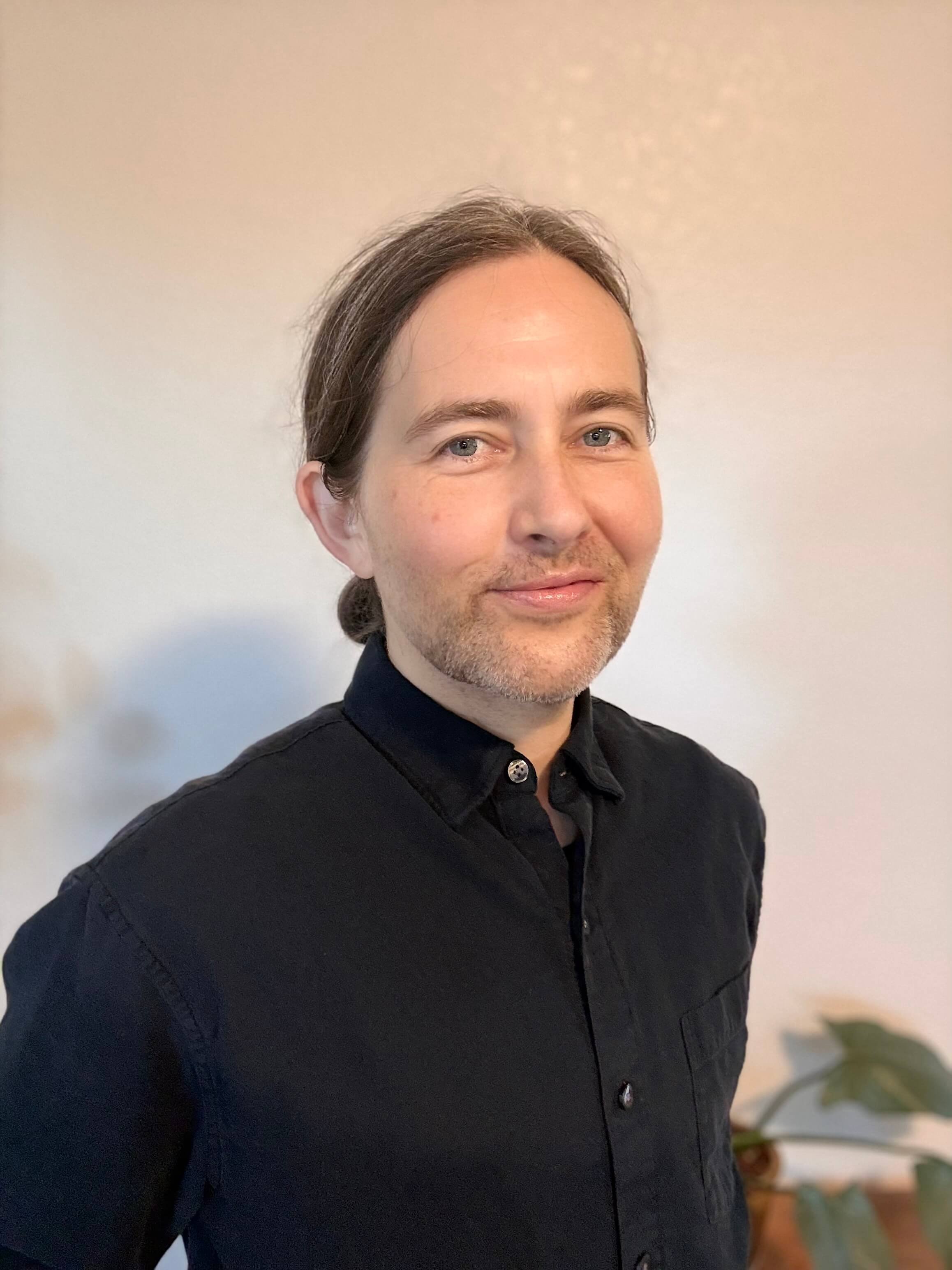Marcel Parker LMFT, trans autistic therapist. Long grey-brown hair, blue eyes, black shirt. Oakland