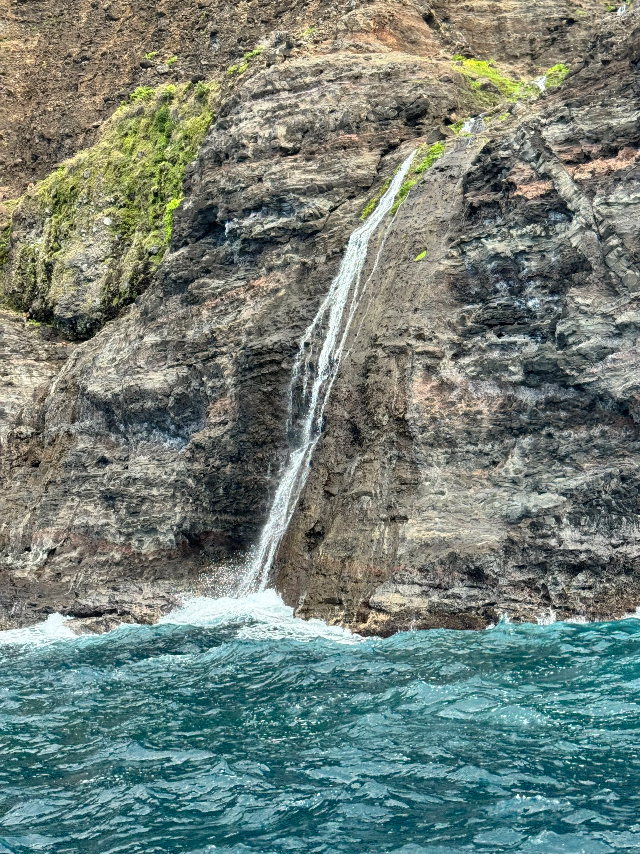A small waterfall flowing down a rocky cliff into the ocean below.