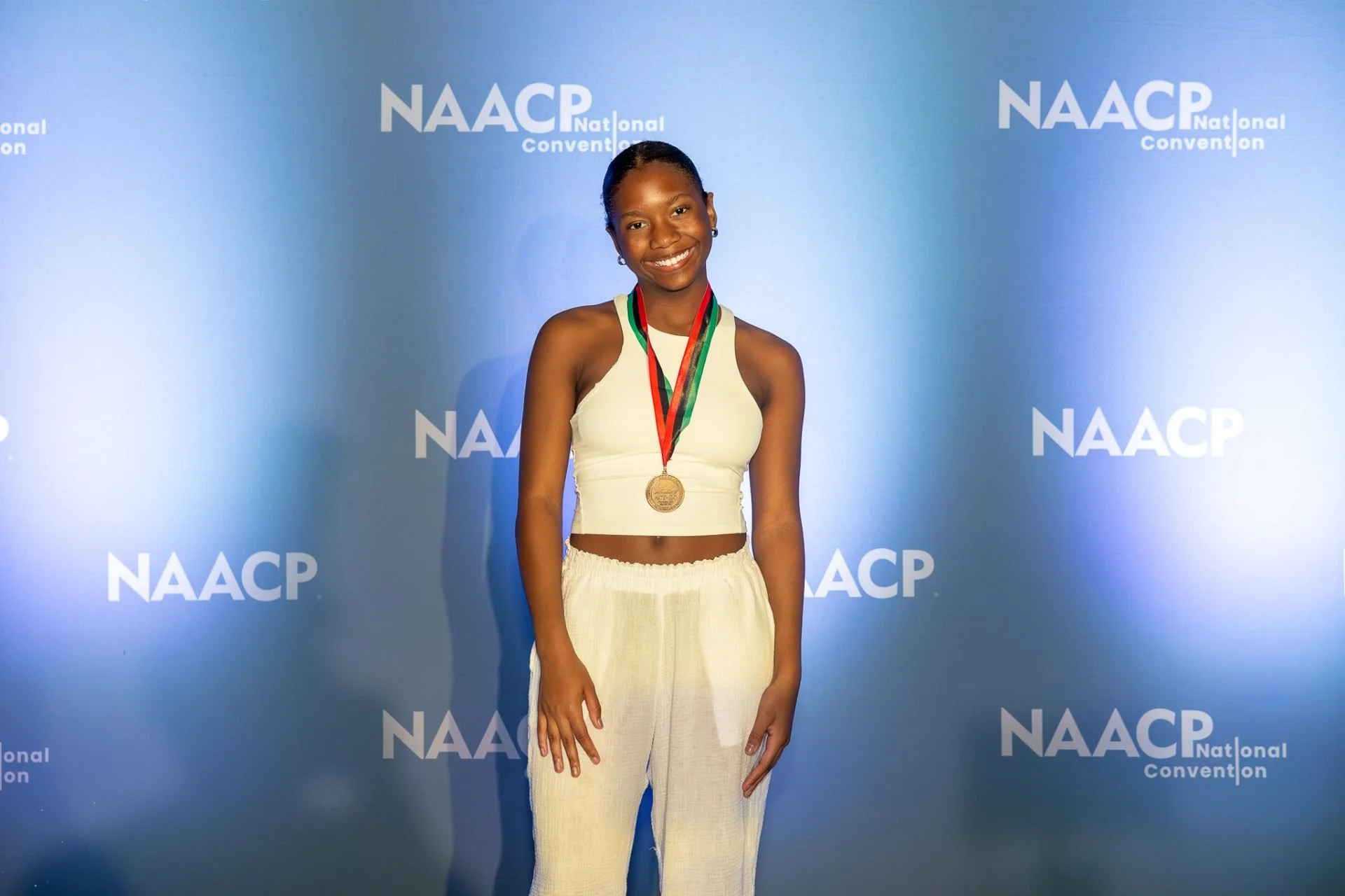 Journey Spencer smiling and wearing a medal in front of an NAACP National Convention backdrop.